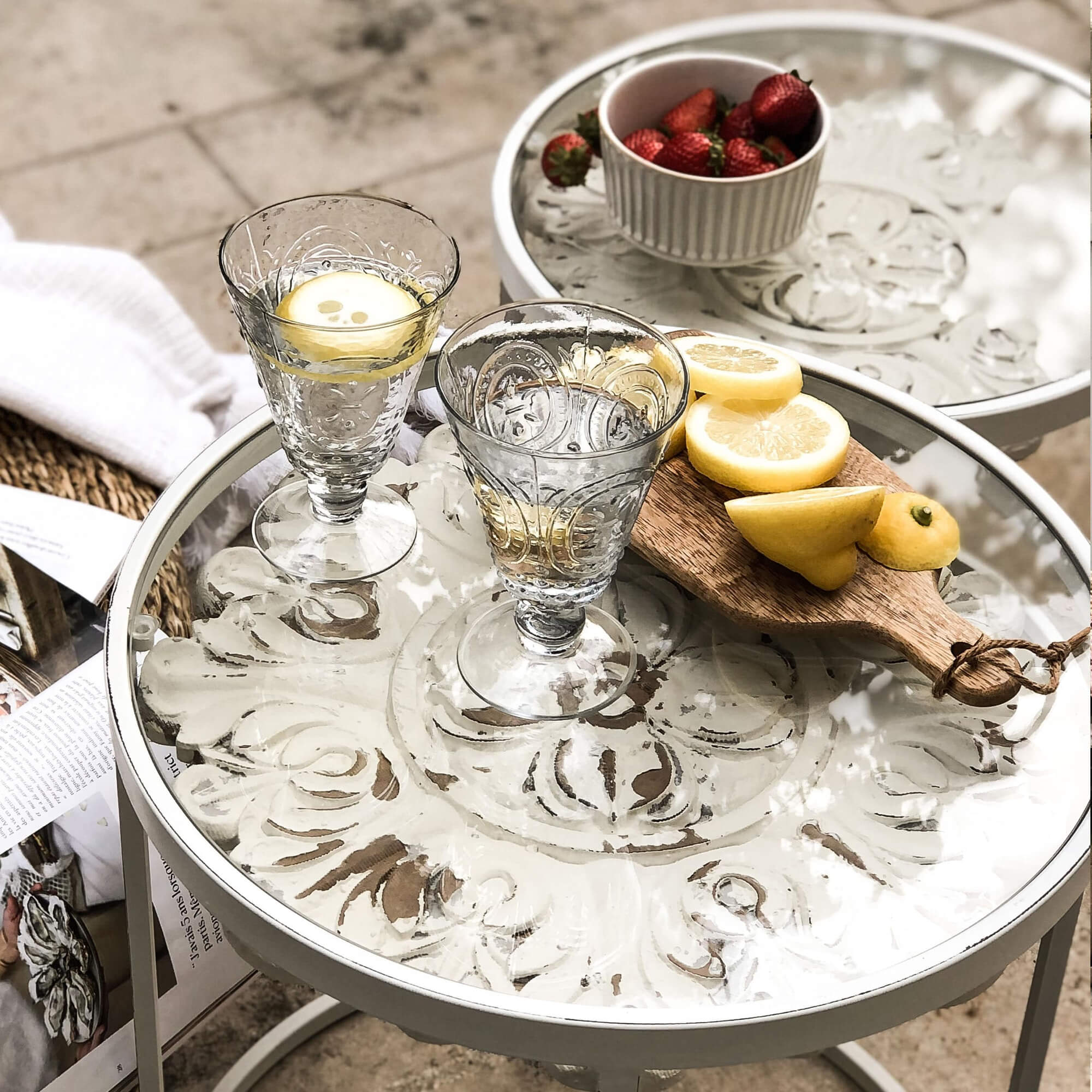 Verres en verre avec eau et citron sur table ronde blanche en métal avec plateau décoratif