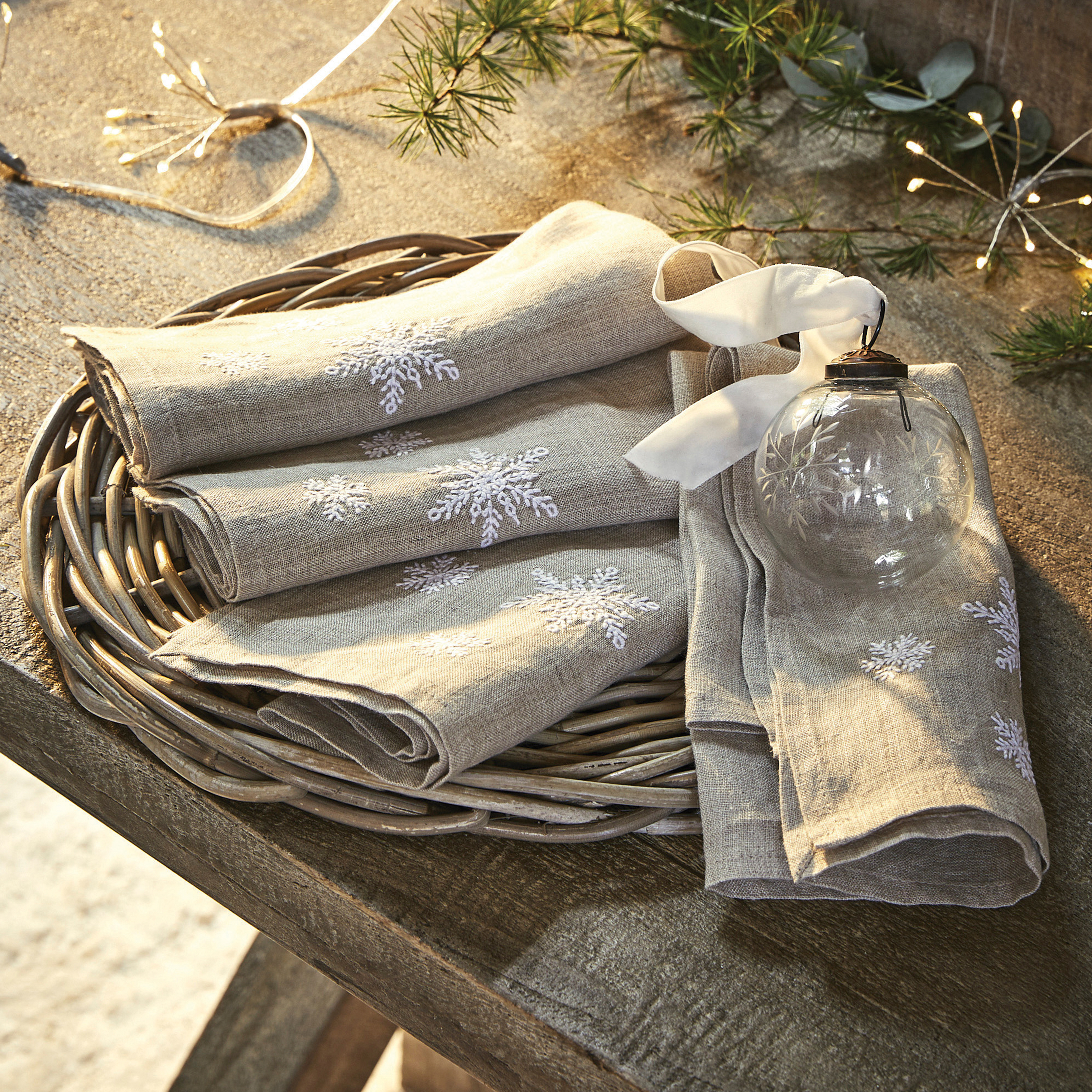 Serviettes en lin beige avec broderie flocons blancs sur plateau en osier, décoration de Noël
