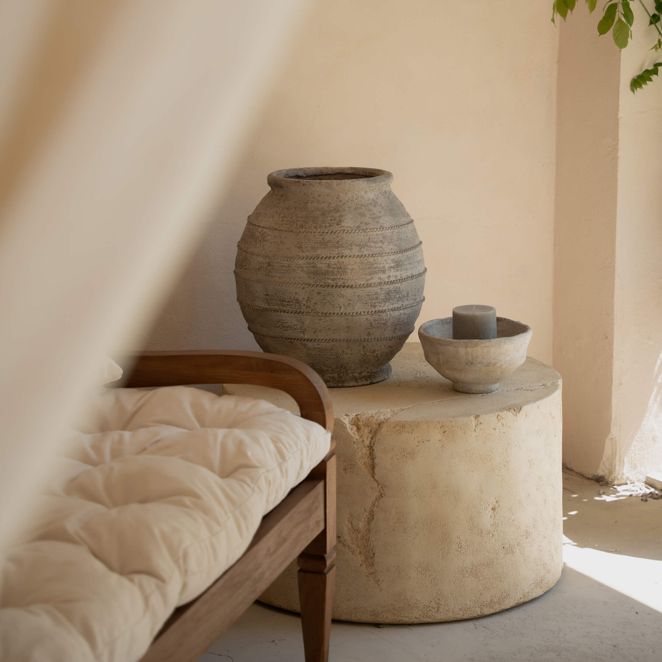Table ronde en pierre avec vase en céramique grise et bougie dans un intérieur clair avec banc en bois