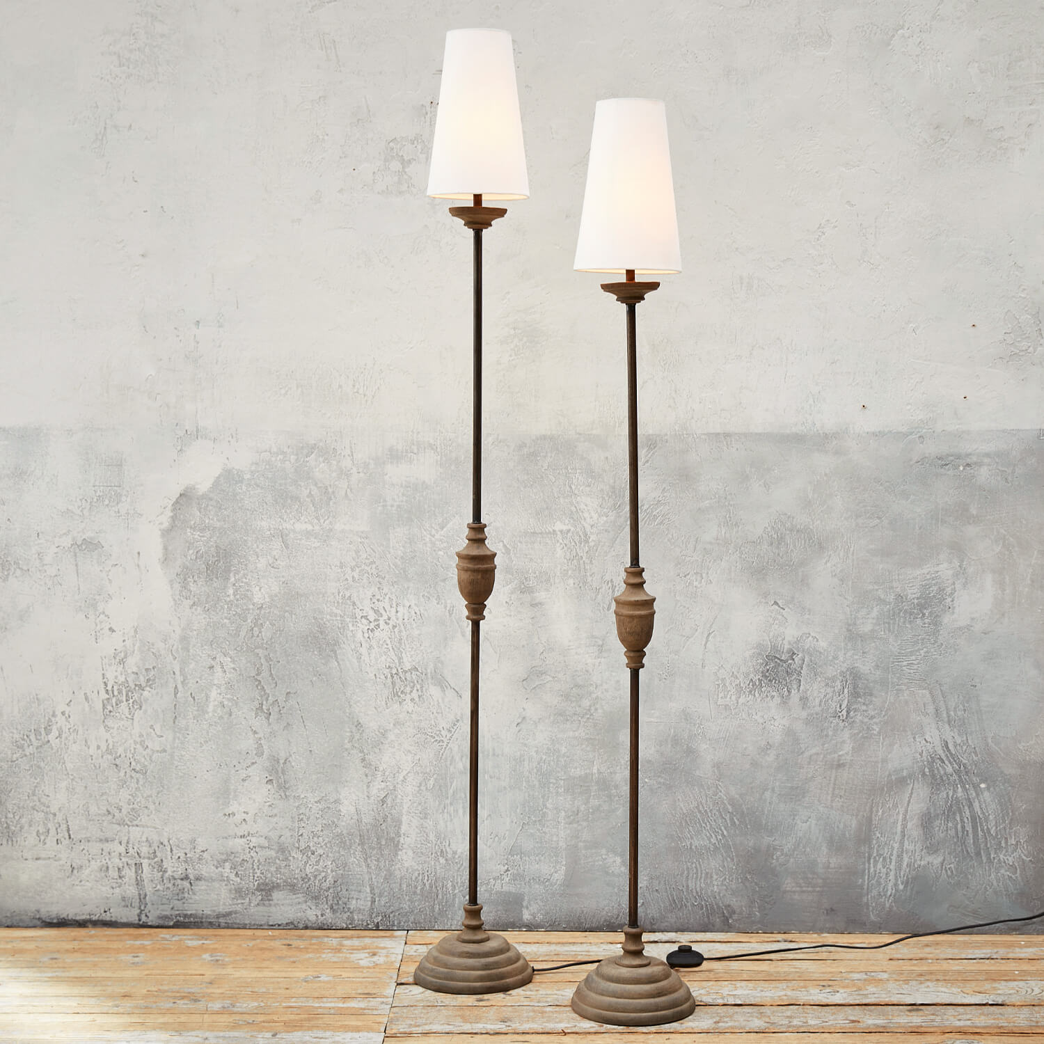 Deux lampadaires hauts avec base en métal et abat-jours blancs sur un sol en bois clair
