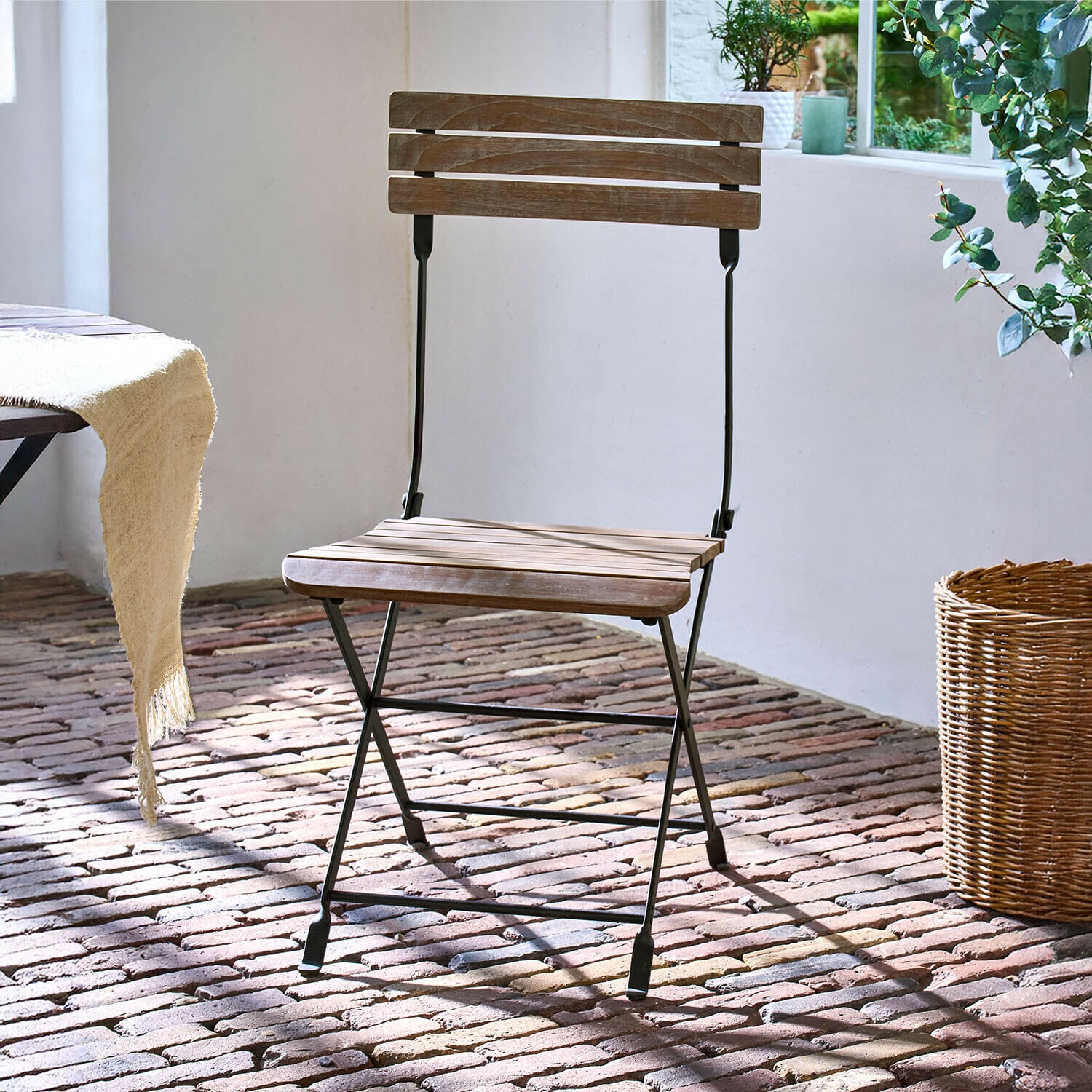 Chaise Arémont Chaise pliante en bois avec structure métallique noire sur sol en briques sous lumière naturelle