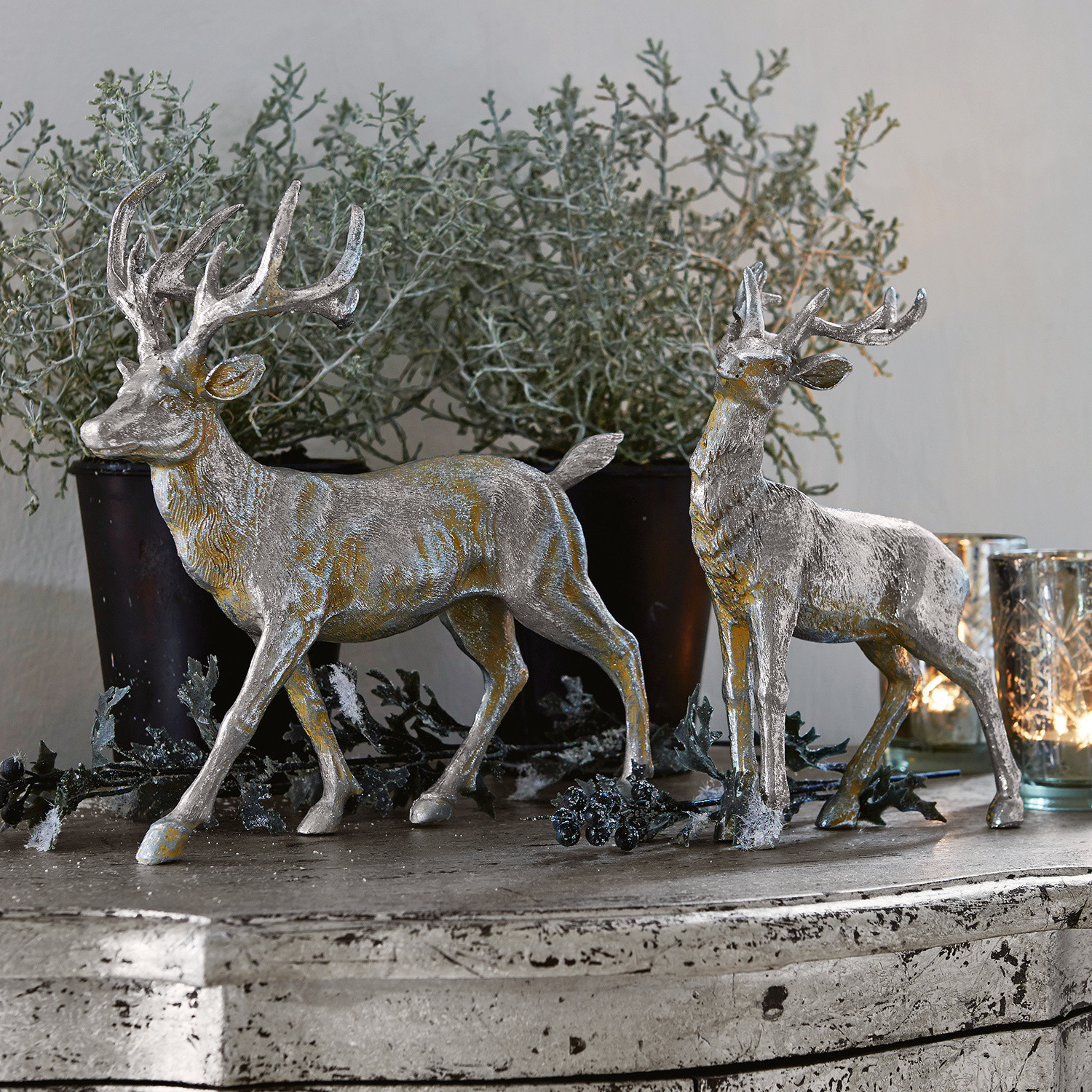 Lot de 2 cerfs Rudy & Son Deux décorations de cerfs argentés en résine sur une commode rustique avec plantes et bougies