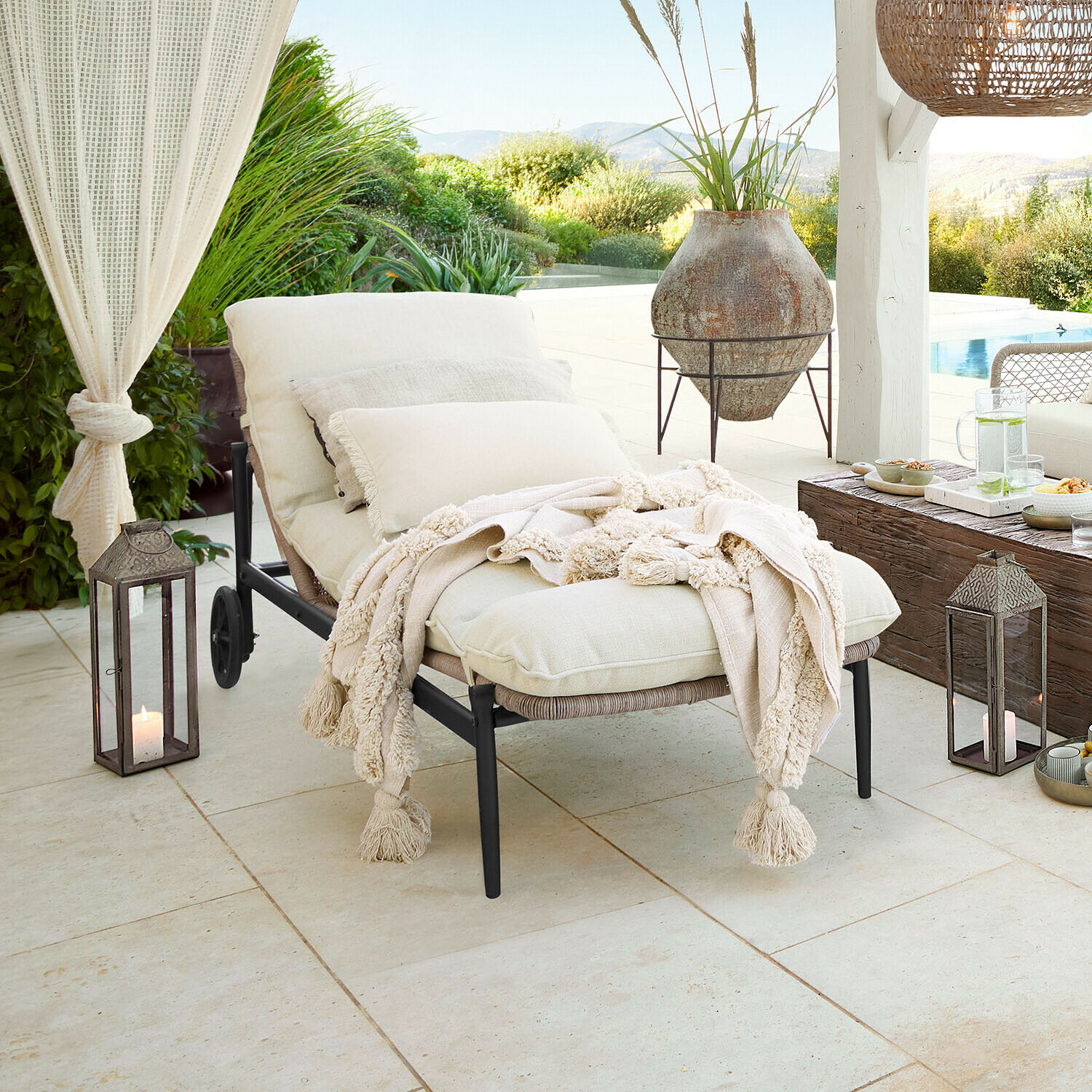 Chaise longue de jardin avec coussins crème et couverture douce sur terrasse avec vue sur piscine et verdure