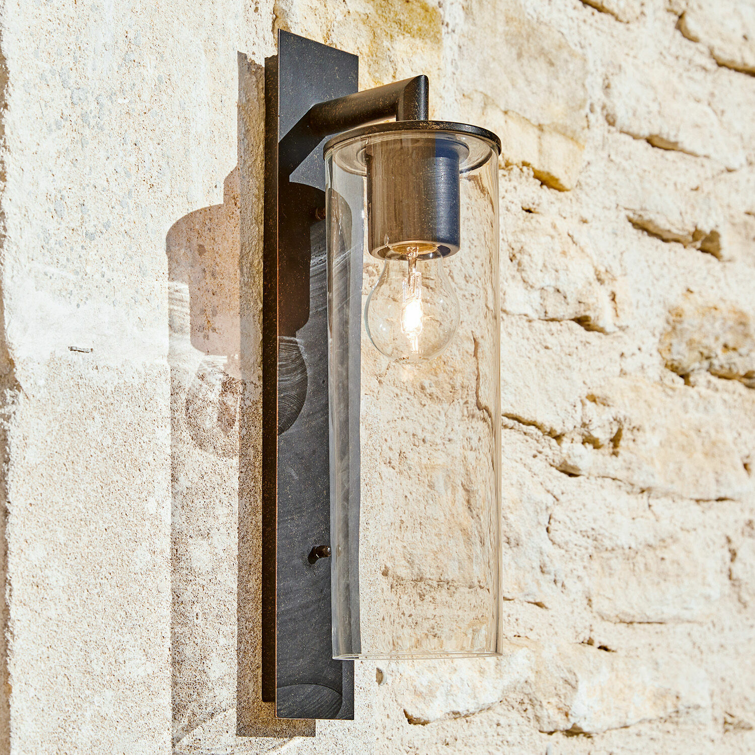 Applique extérieure Clisson Applique murale noire en métal avec abat-jour en verre transparent sur mur en pierre clair