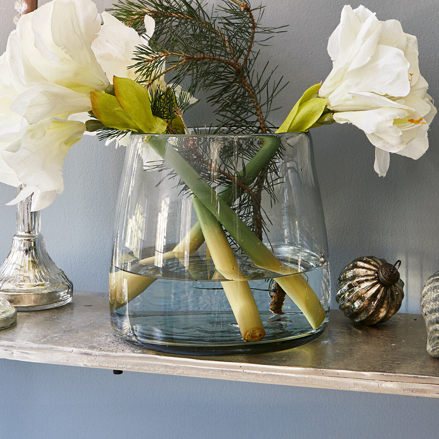 Vase Inga Vase en verre transparent avec fleurs blanches et branches vertes sur une étagère décorative