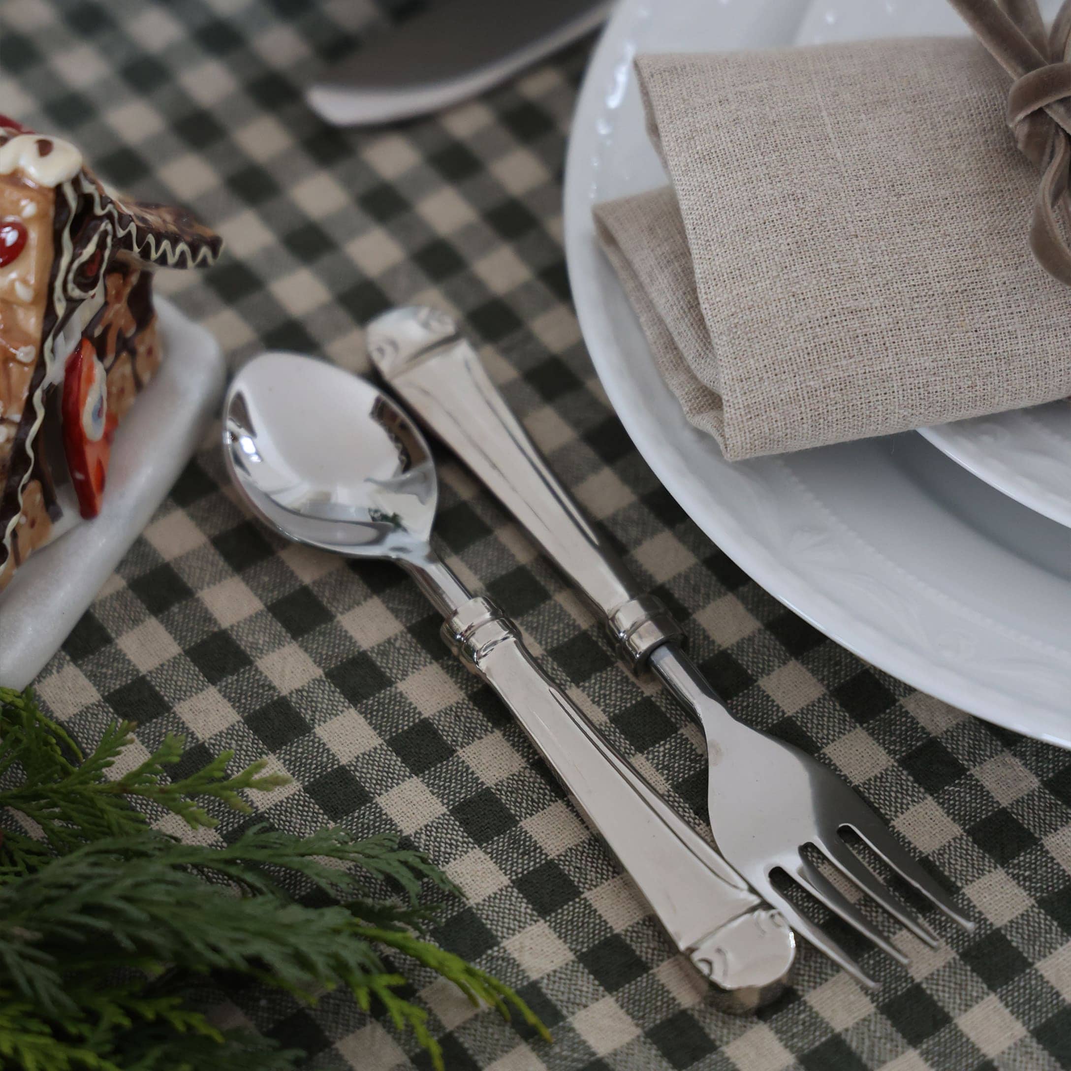 Cuillère et fourchette en argent sur nappe à carreaux verts avec serviette en lin beige et assiette blanche