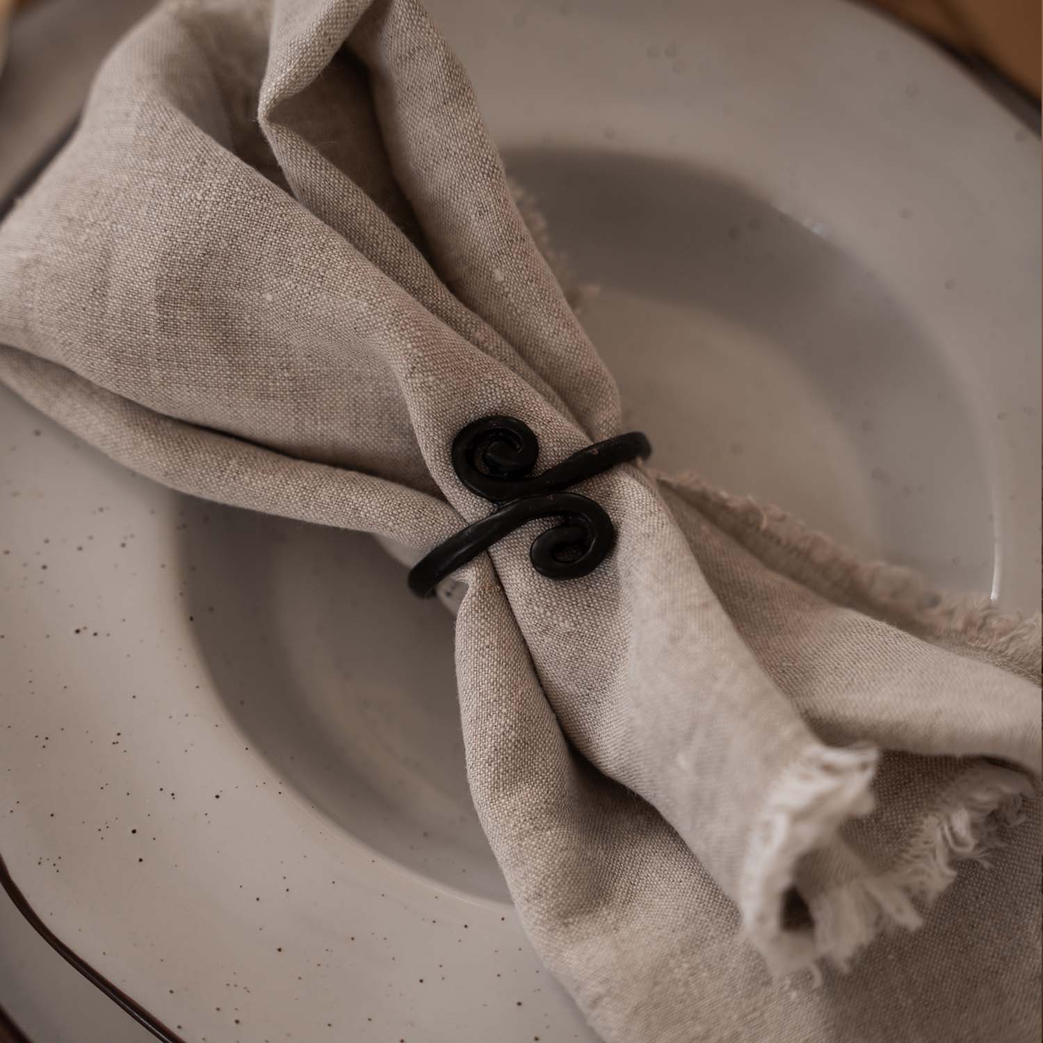 Serviette en lin beige avec anneau en métal noir sur une assiette claire