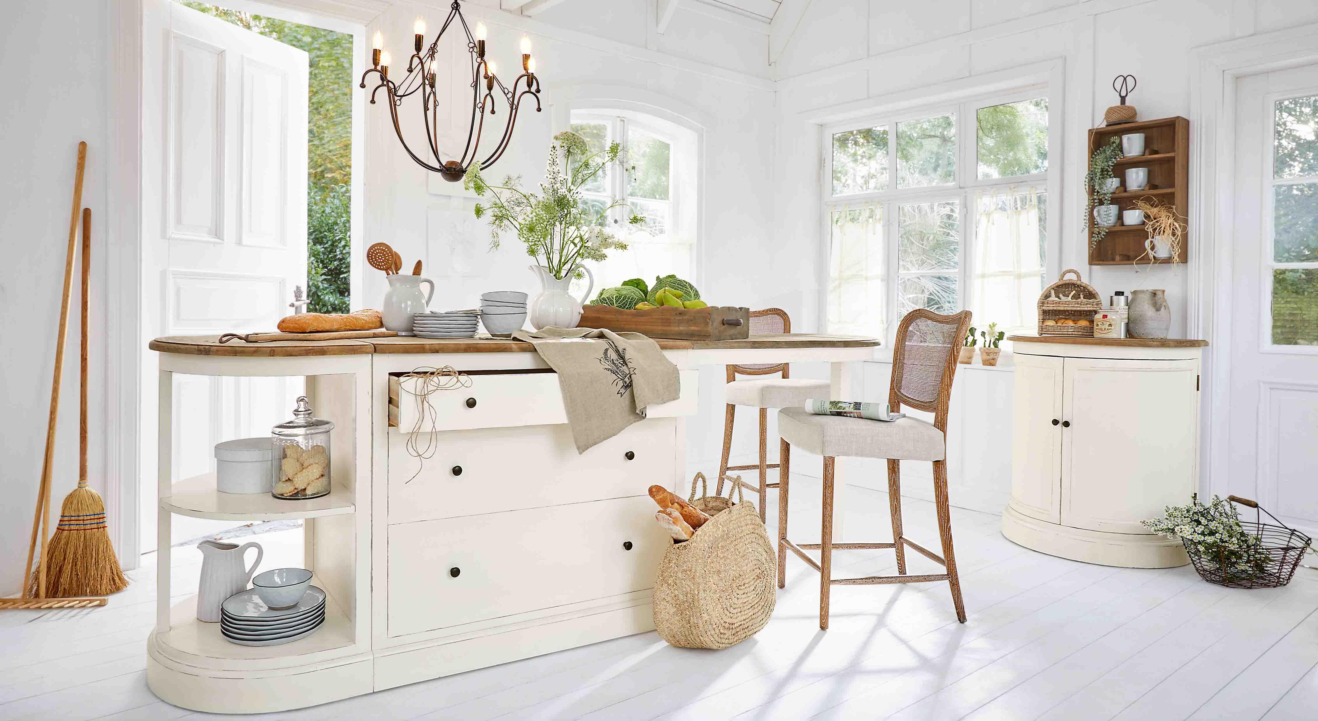 Cuisine lumineuse avec îlot blanc à plateau en bois et chaises en osier, décorations naturelles