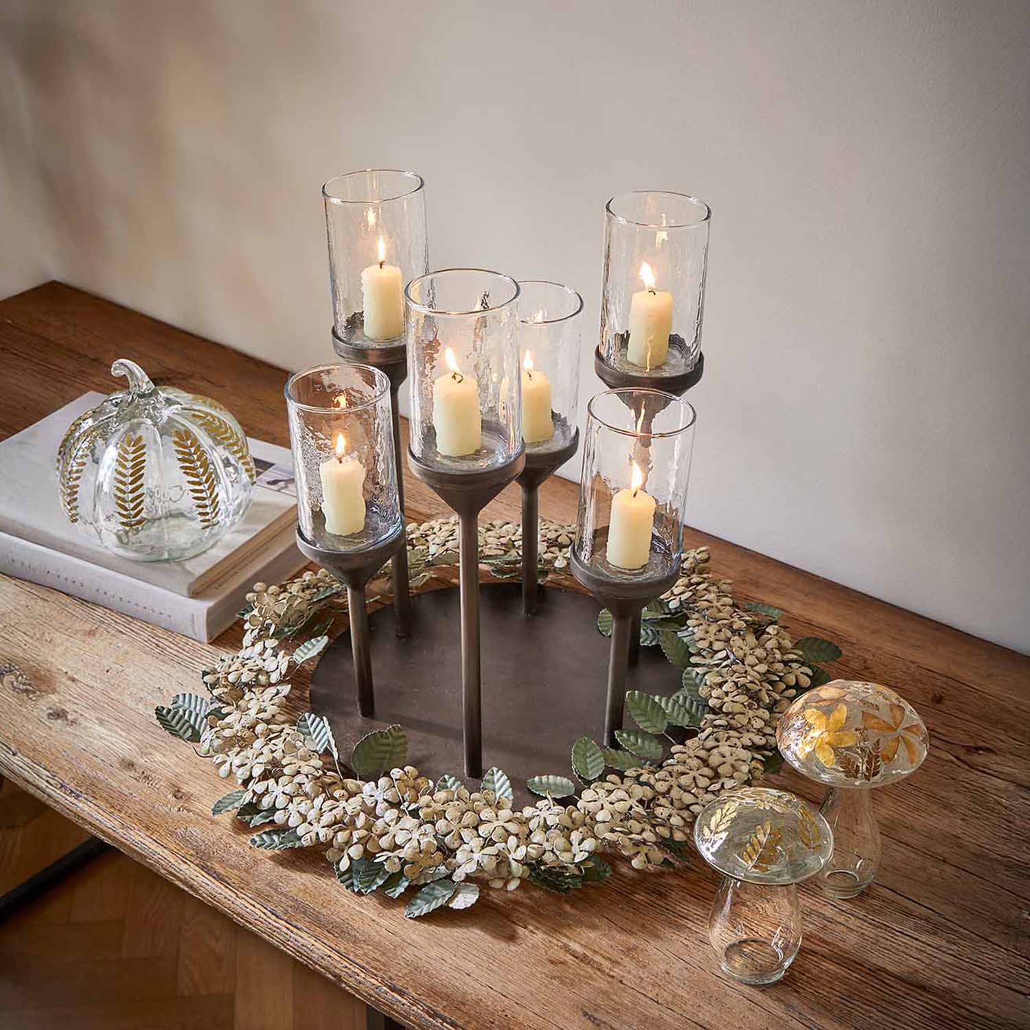 Bougeoir en métal avec six verres et bougies blanches sur une table en bois décorée de fleurs