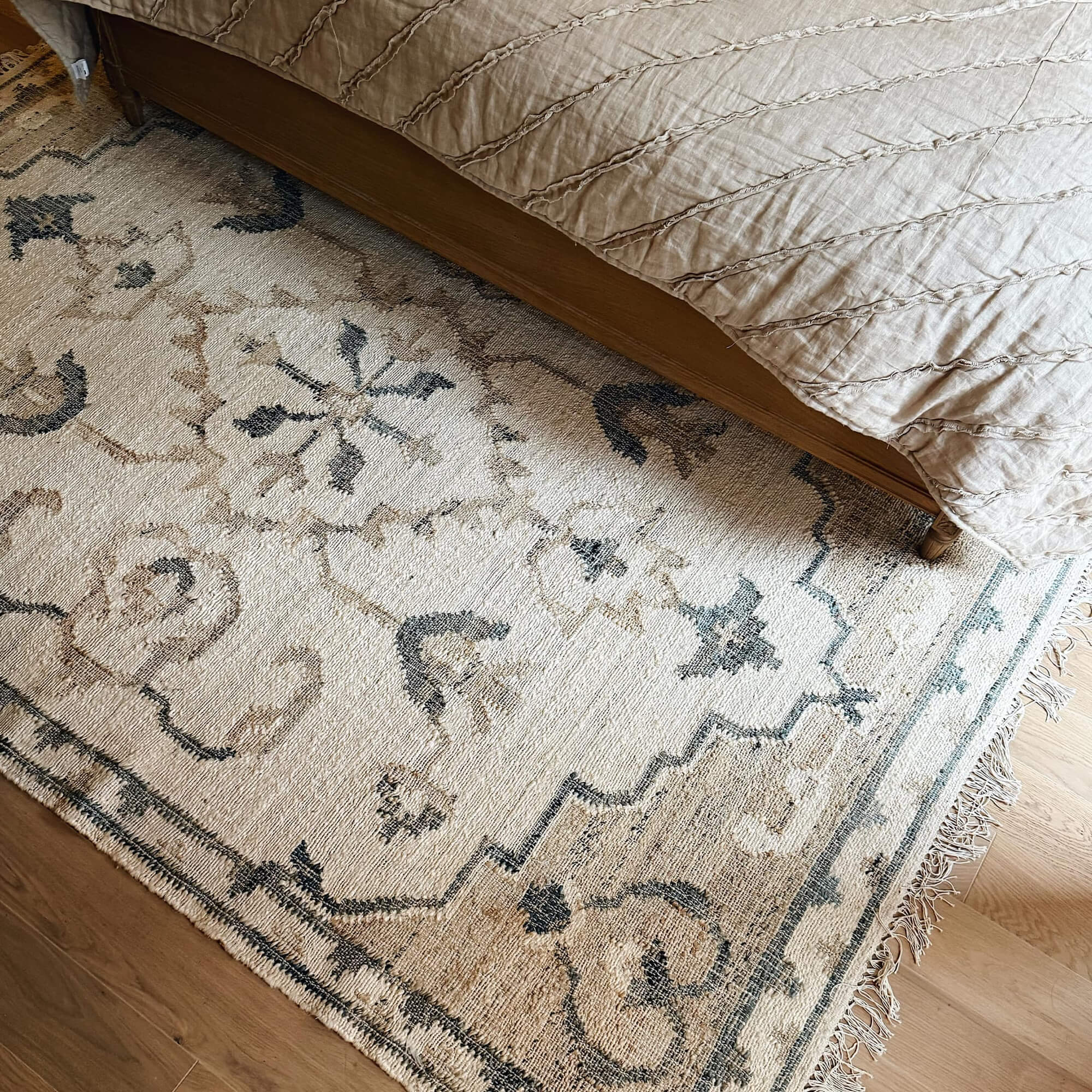 Tapis beige à motif oriental avec franges sous un lit en bois dans une chambre à coucher
