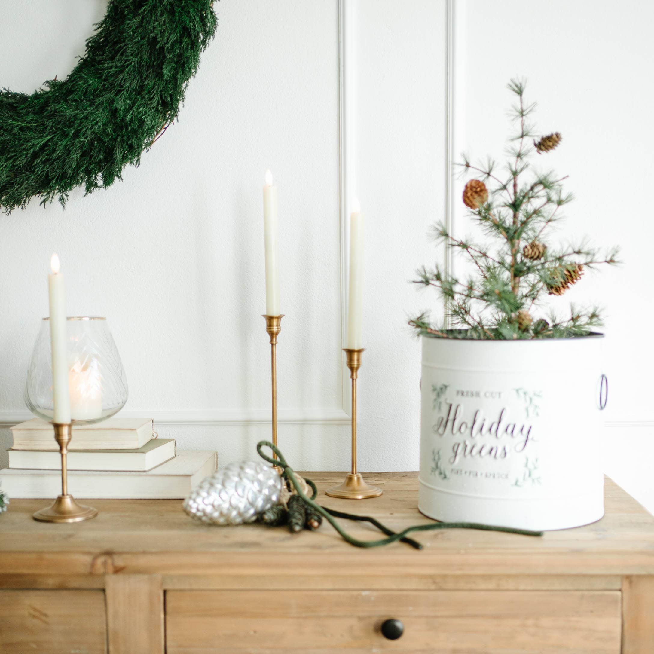 Décoration de Noël avec couronne verte, bougeoirs dorés et pot blanc avec branches et pommes de pin
