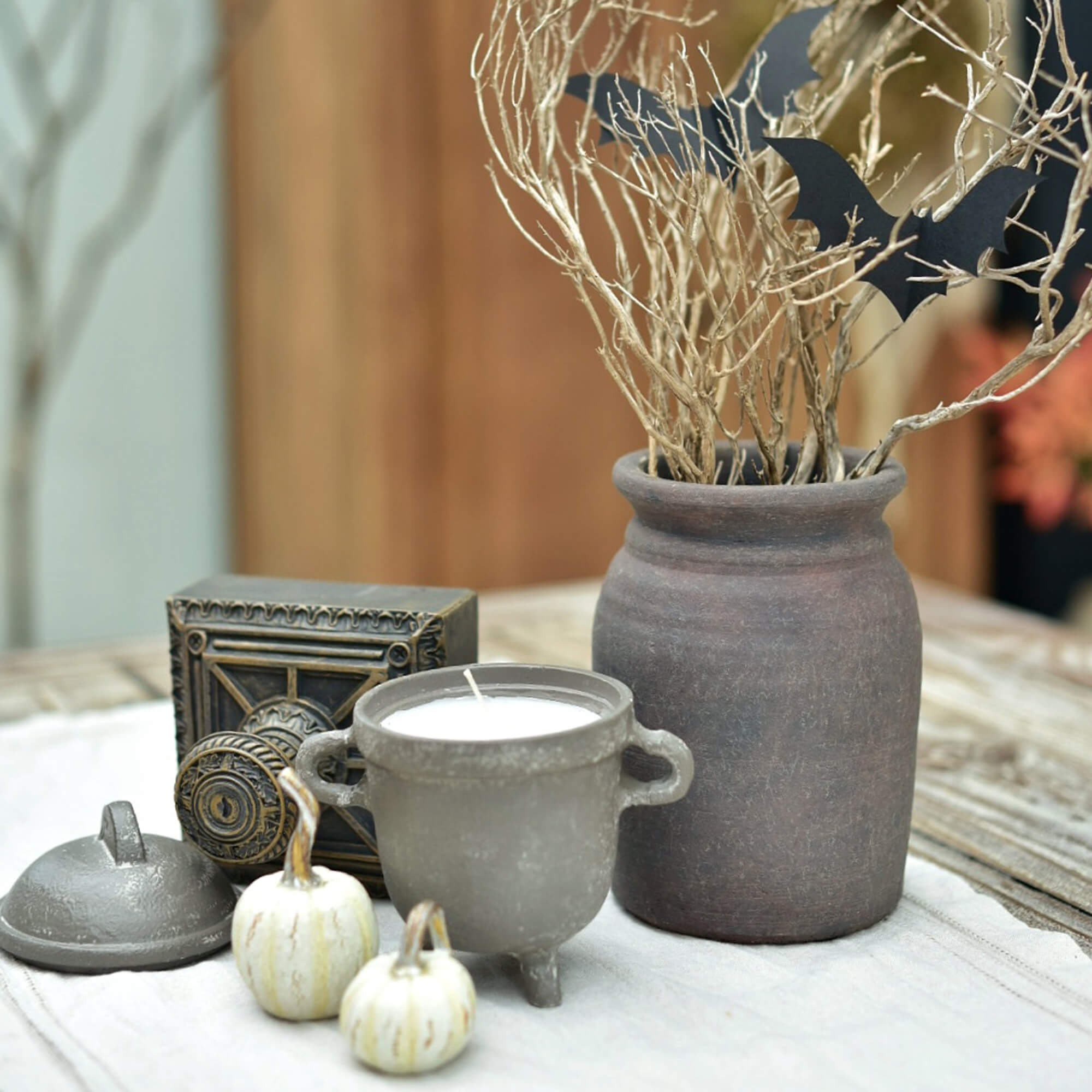 Ensemble décoratif avec bougie en céramique, vase en argile et petites citrouilles blanches sur table