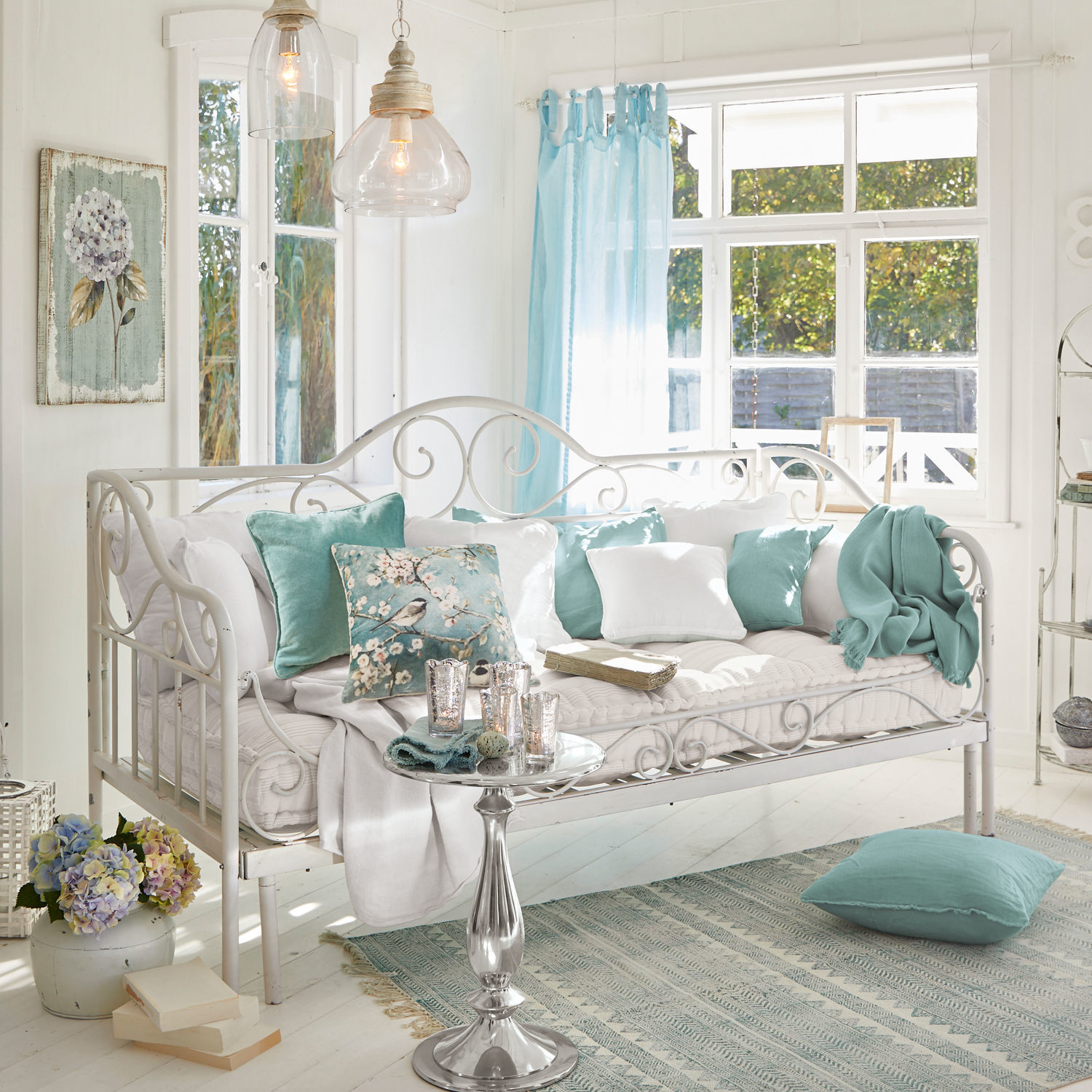 Banquette Maditha Canapé en métal blanc avec coussins doux et accents turquoise dans un salon lumineux avec grande fenêtre