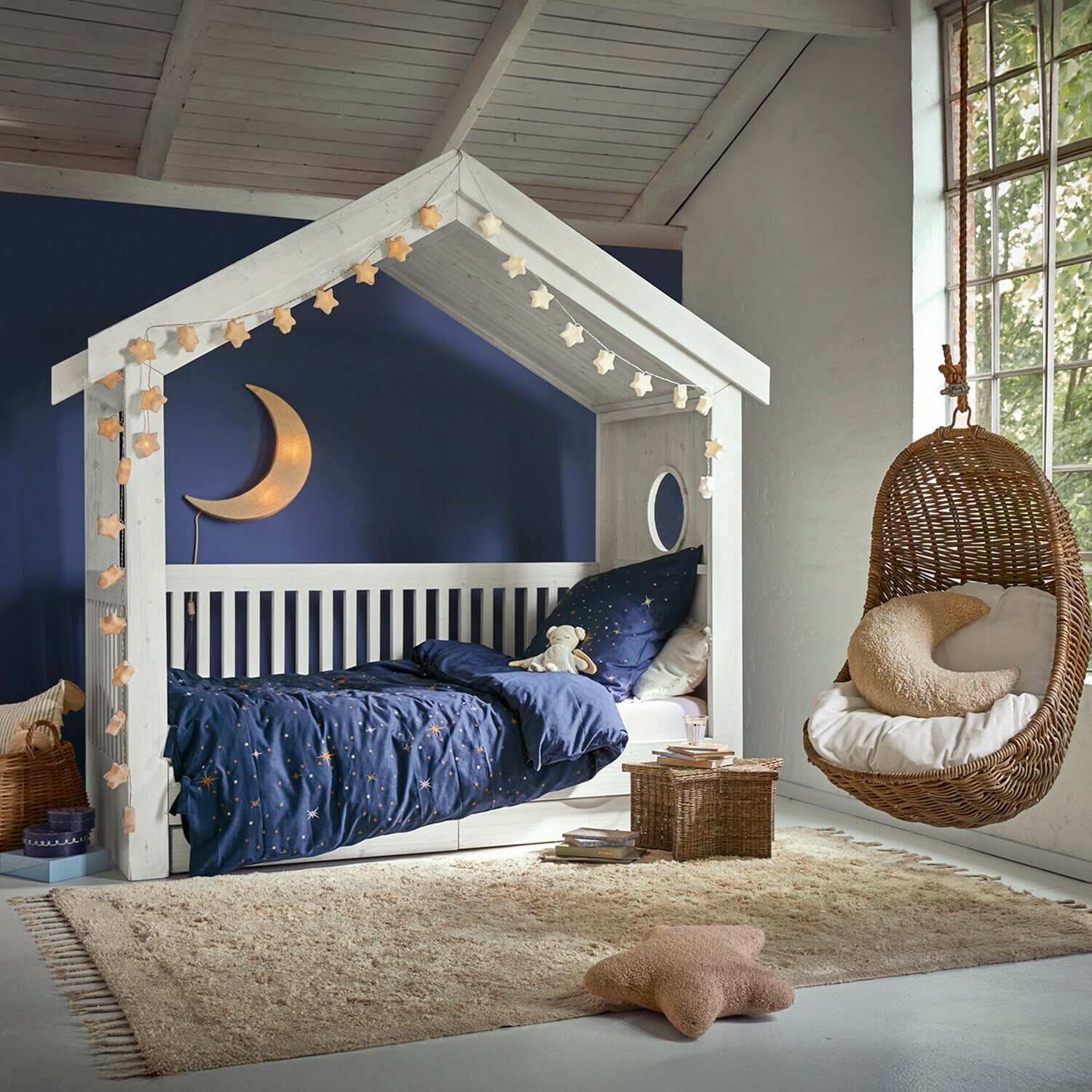 Tapis Avenagh Lit en bois blanc en forme de maison avec literie bleue étoilée et fauteuil suspendu en osier dans une chambre enfant