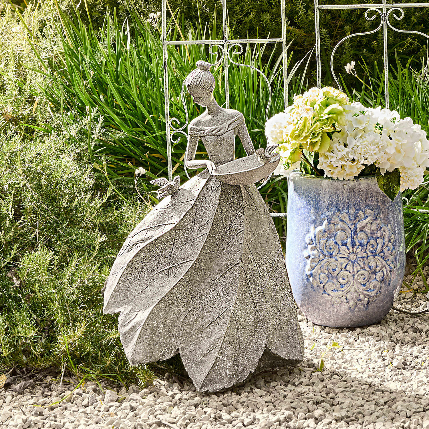 Sculpture Sullon Décoration de jardin en pierre grise représentant une femme avec une robe en feuilles sur un sol de gravier