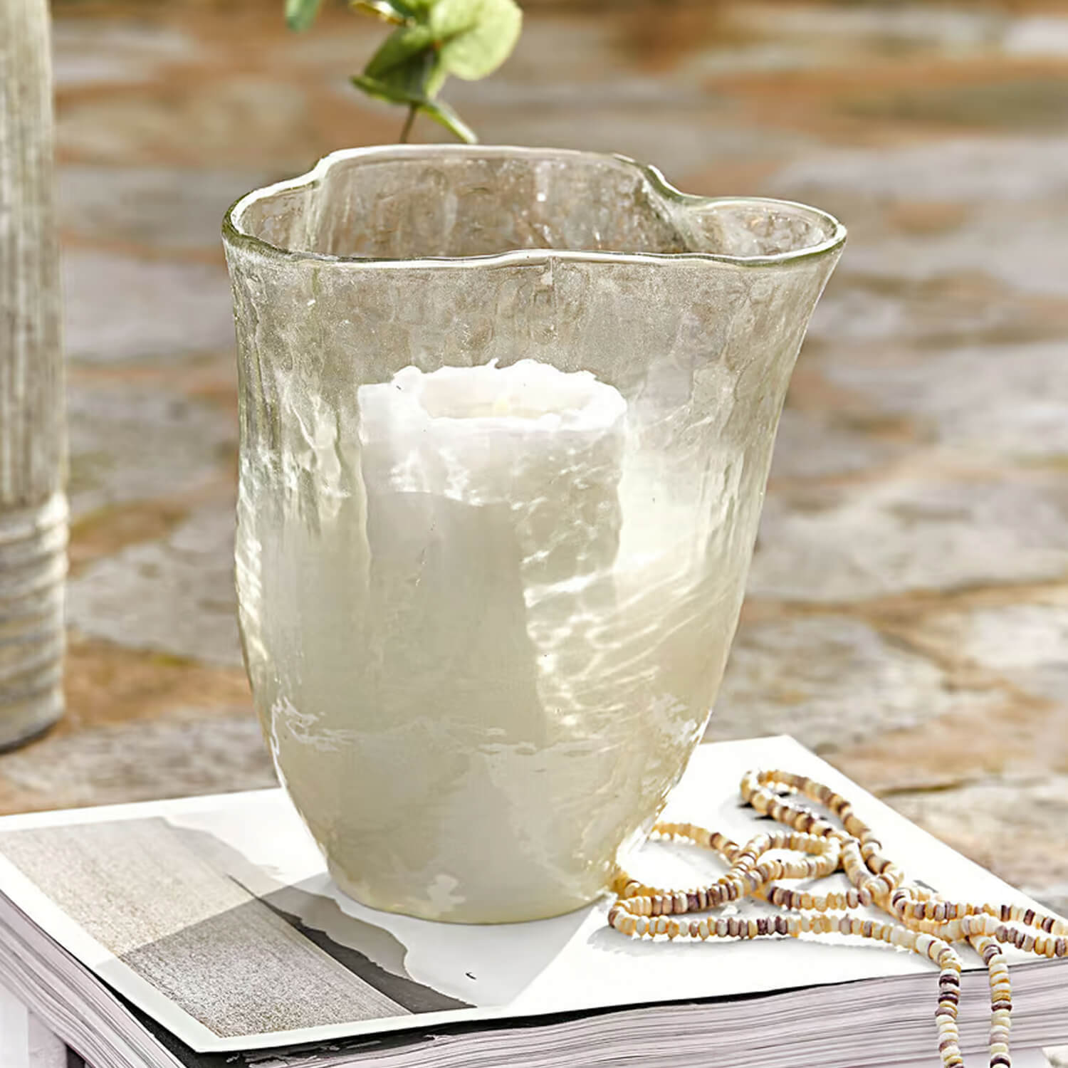Photophore en verre transparent avec bougie blanche posé sur un livre avec un collier décoratif