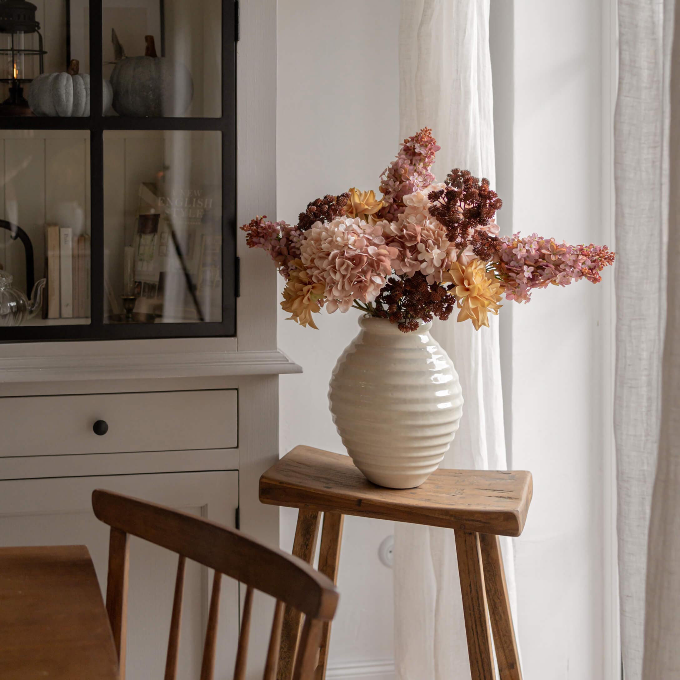 Vase en albâtre blanc avec fleurs jaunes et roses sur un tabouret en bois dans un intérieur lumineux