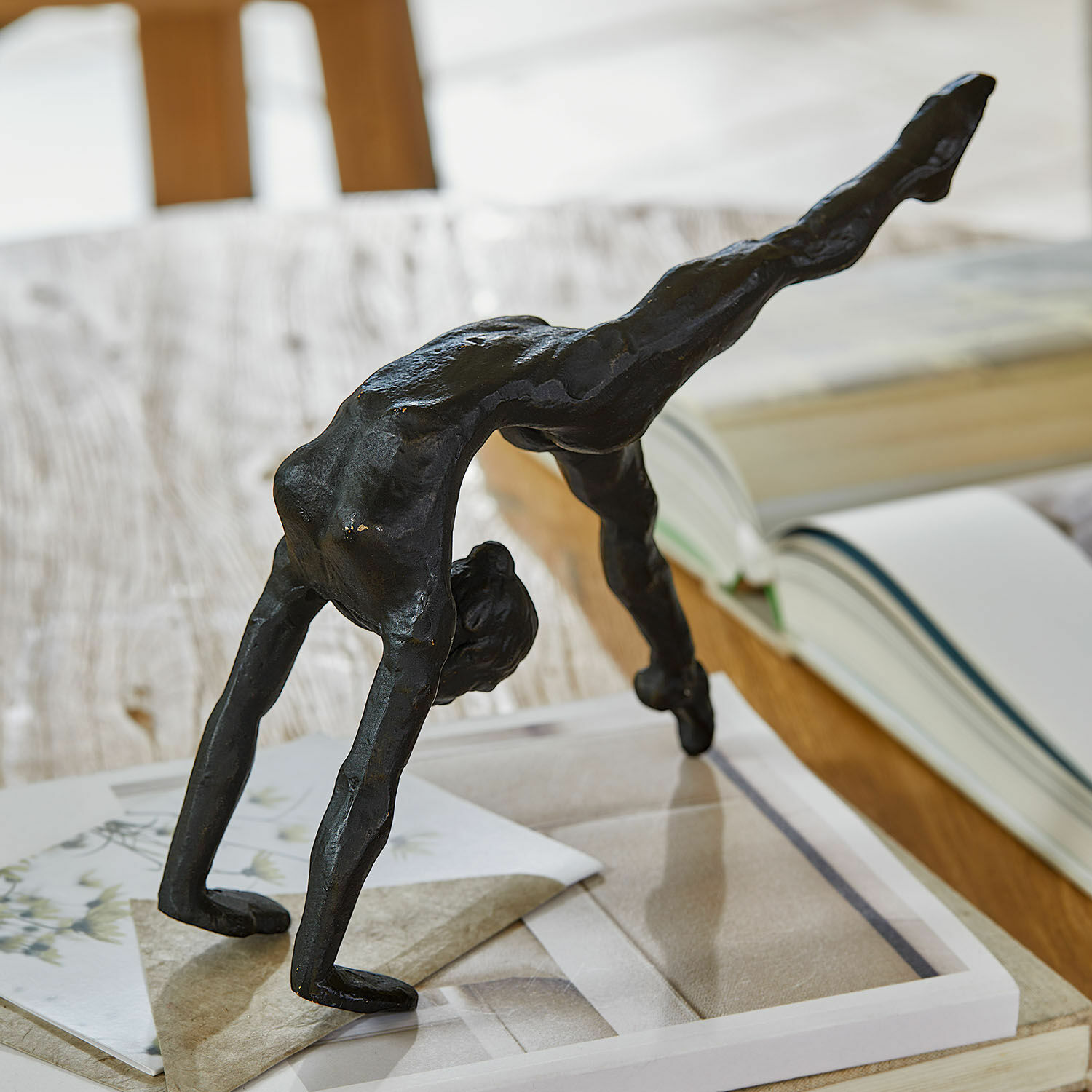 Statuette Zayrah Figurine noire en métal d'un acrobate en pont sur une table avec livres et papiers