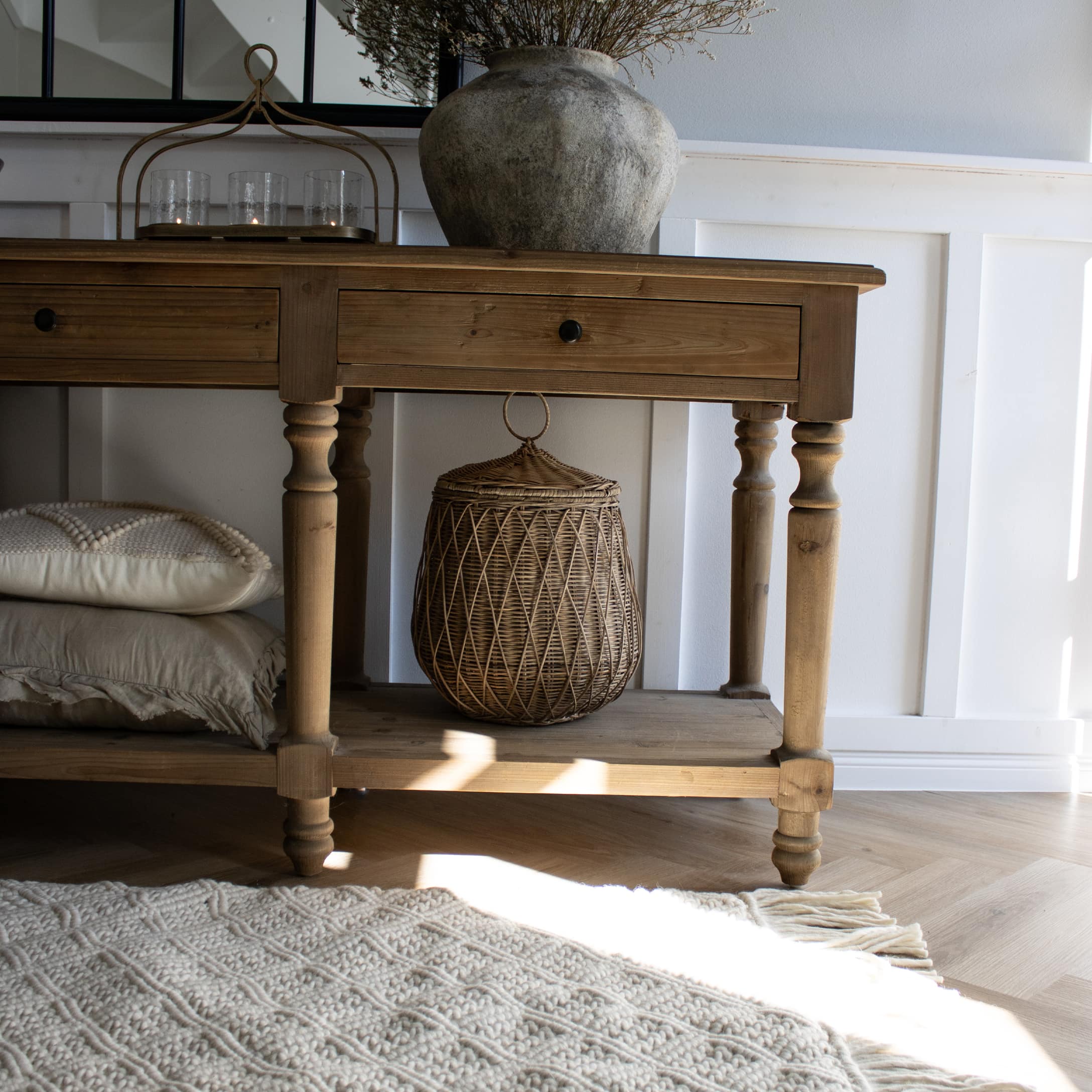 Table en bois avec tiroirs et panier en osier sur l'étagère inférieure, tapis clair à franges