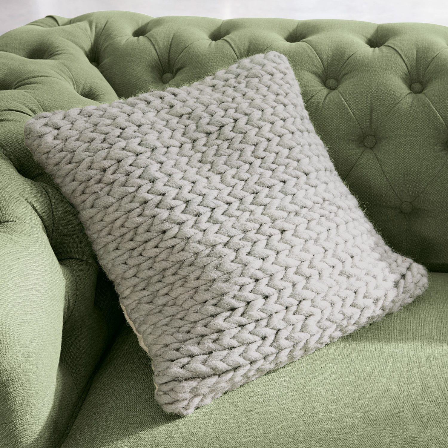Housse de coussin Limnia Coussin beige en grosse maille en laine douce sur un canapé vert capitonné