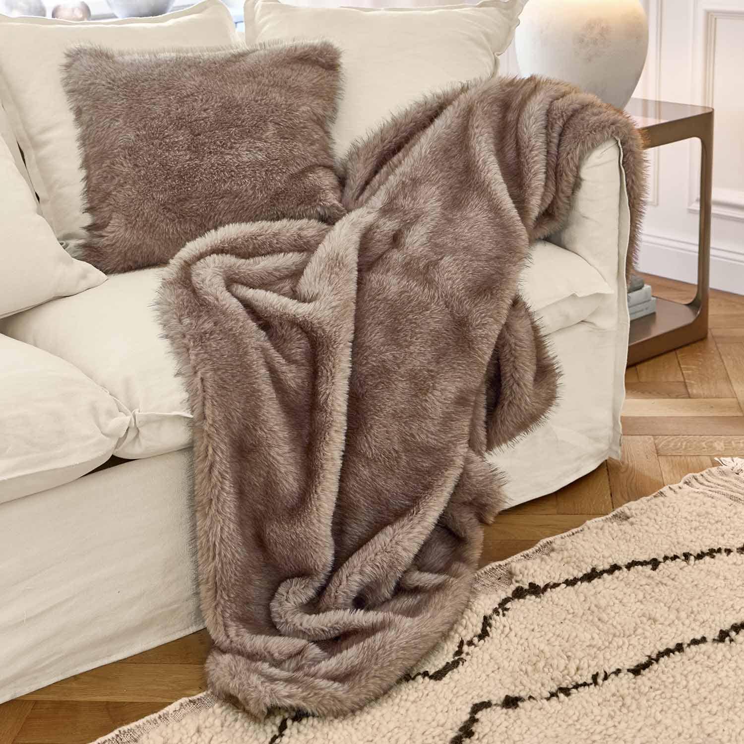 Plaid et coussin en fausse fourrure marron sur canapé blanc dans un salon chaleureux