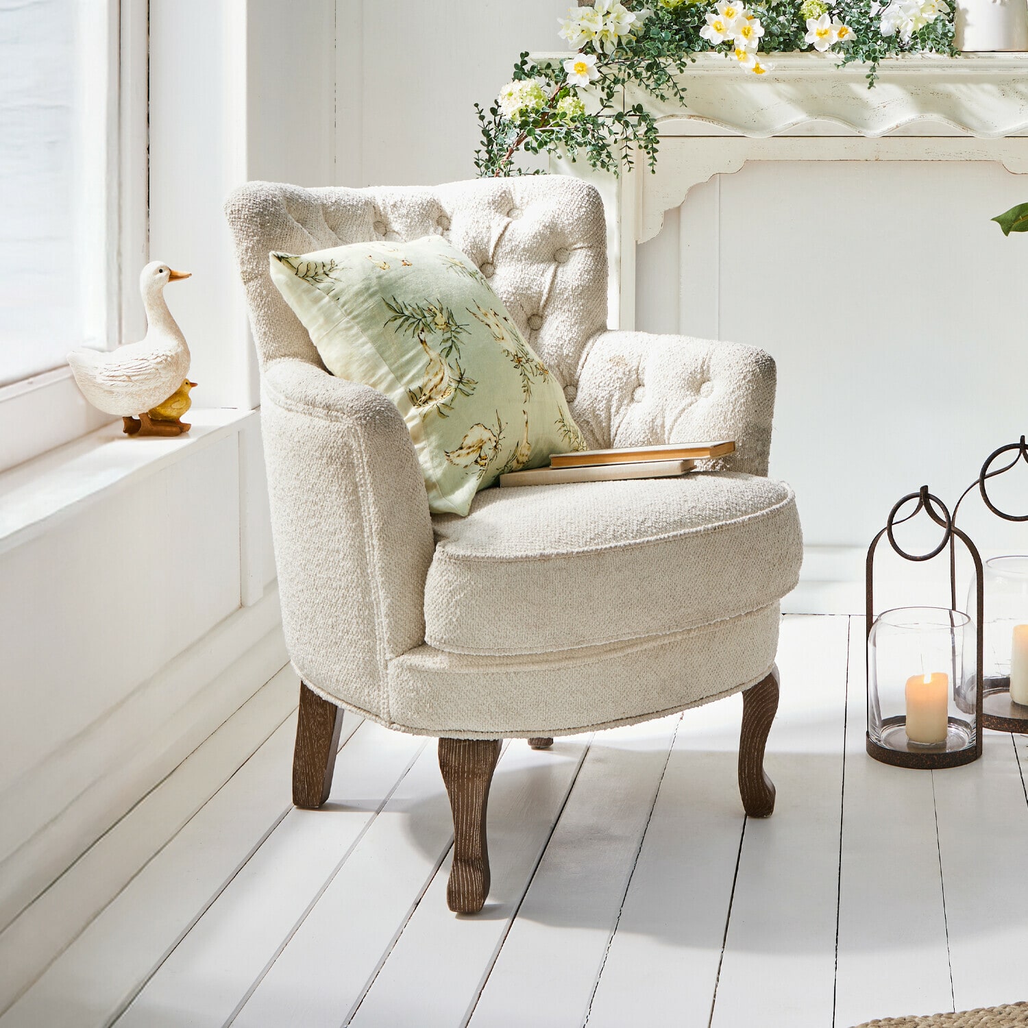 Fauteuil Calgary Fauteuil beige en tissu doux avec pieds en bois et coussin vert à motifs floraux dans un intérieur lumineux