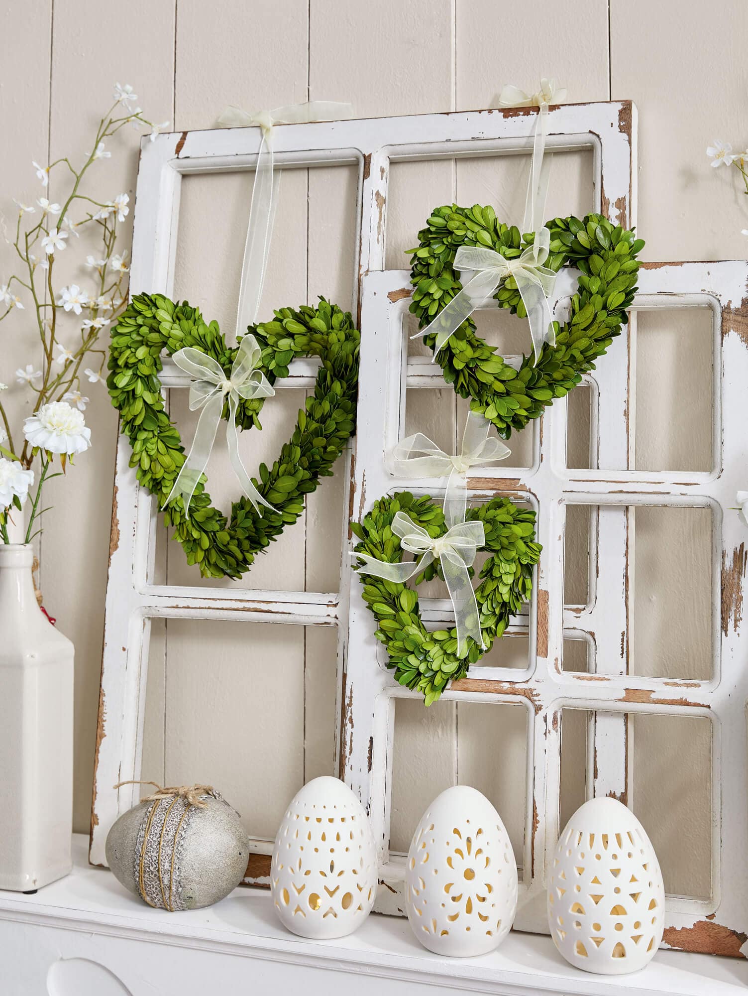 Cœurs verts en feuilles avec nœuds crème suspendus sur cadres de fenêtres blancs vieillissants avec œufs décoratifs