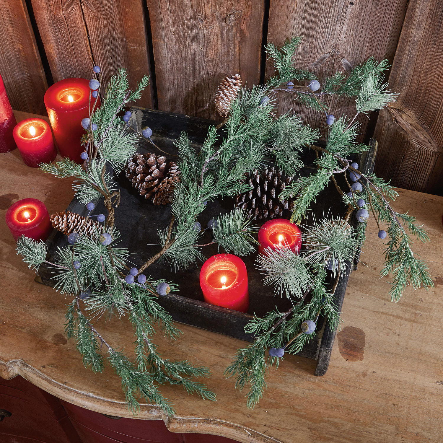 Guirlande Virpi Couronne décorative en branches vertes, pommes de pin et bougies rouges sur une table en bois