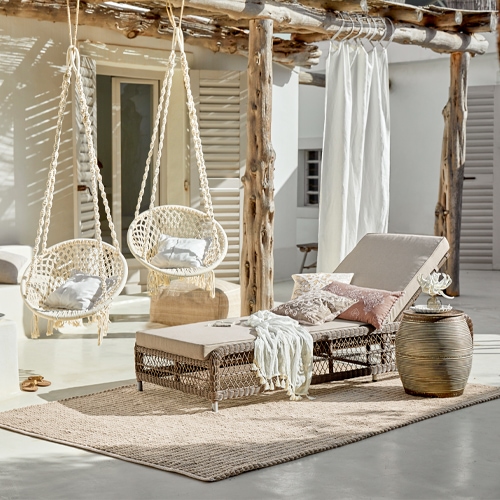 Chaise longue beige avec coussin et table tressée sur tapis clair dans un cadre naturel lumineux