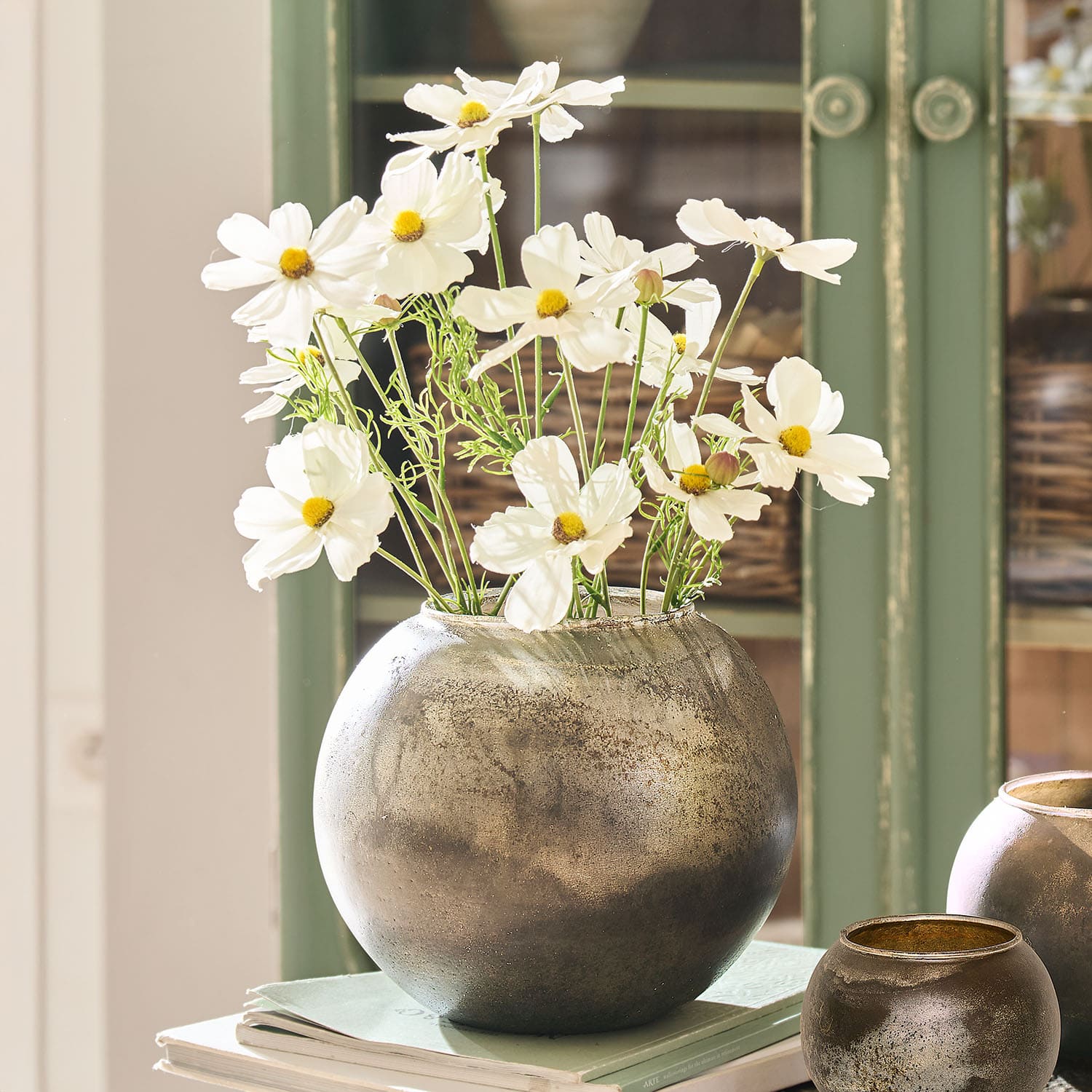 Vase rond en métal argenté avec fleurs blanches posé sur des livres, décoration intérieure élégante