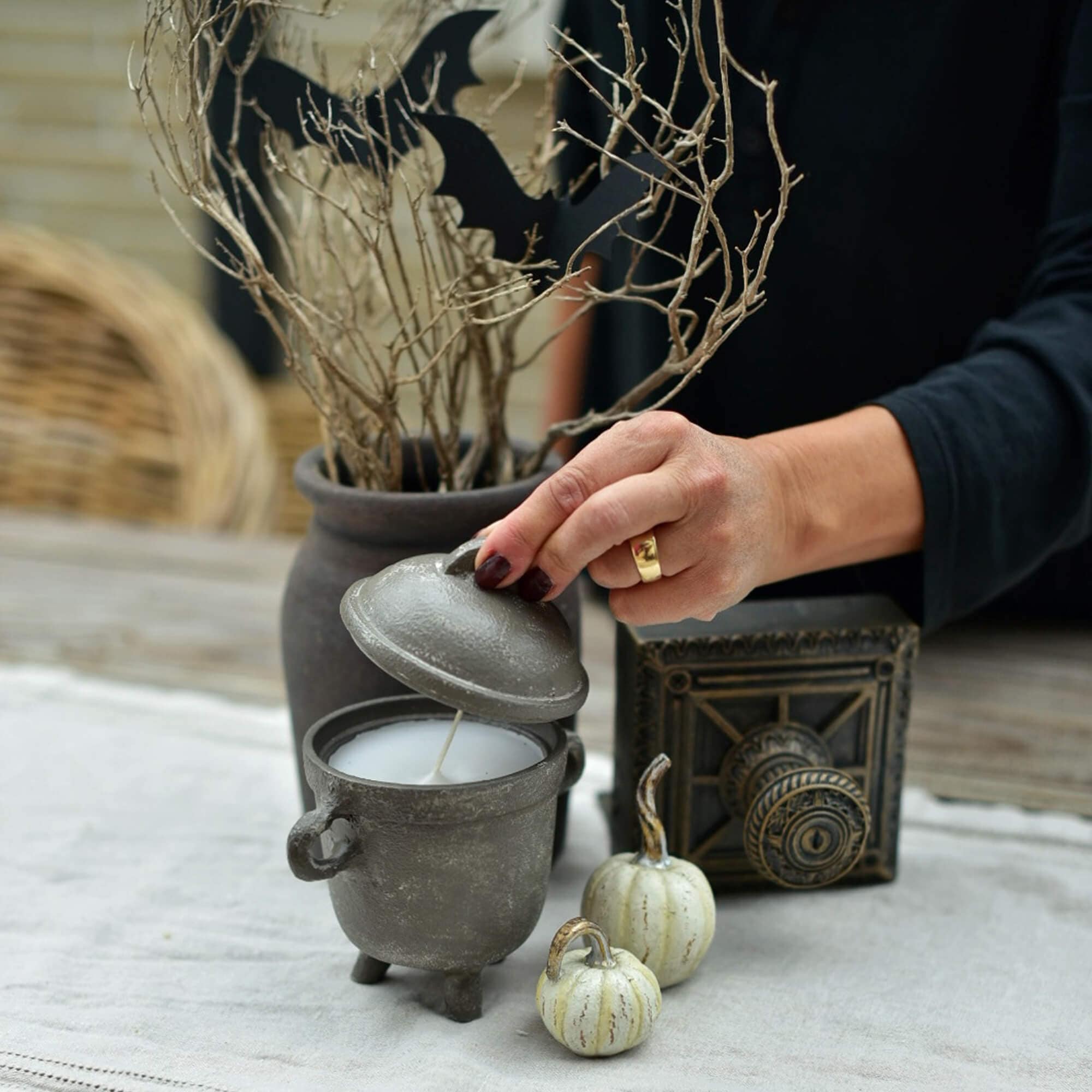 Bougie grise en forme de chaudron avec couvercle sur table décorée pour Halloween avec citrouilles et branches