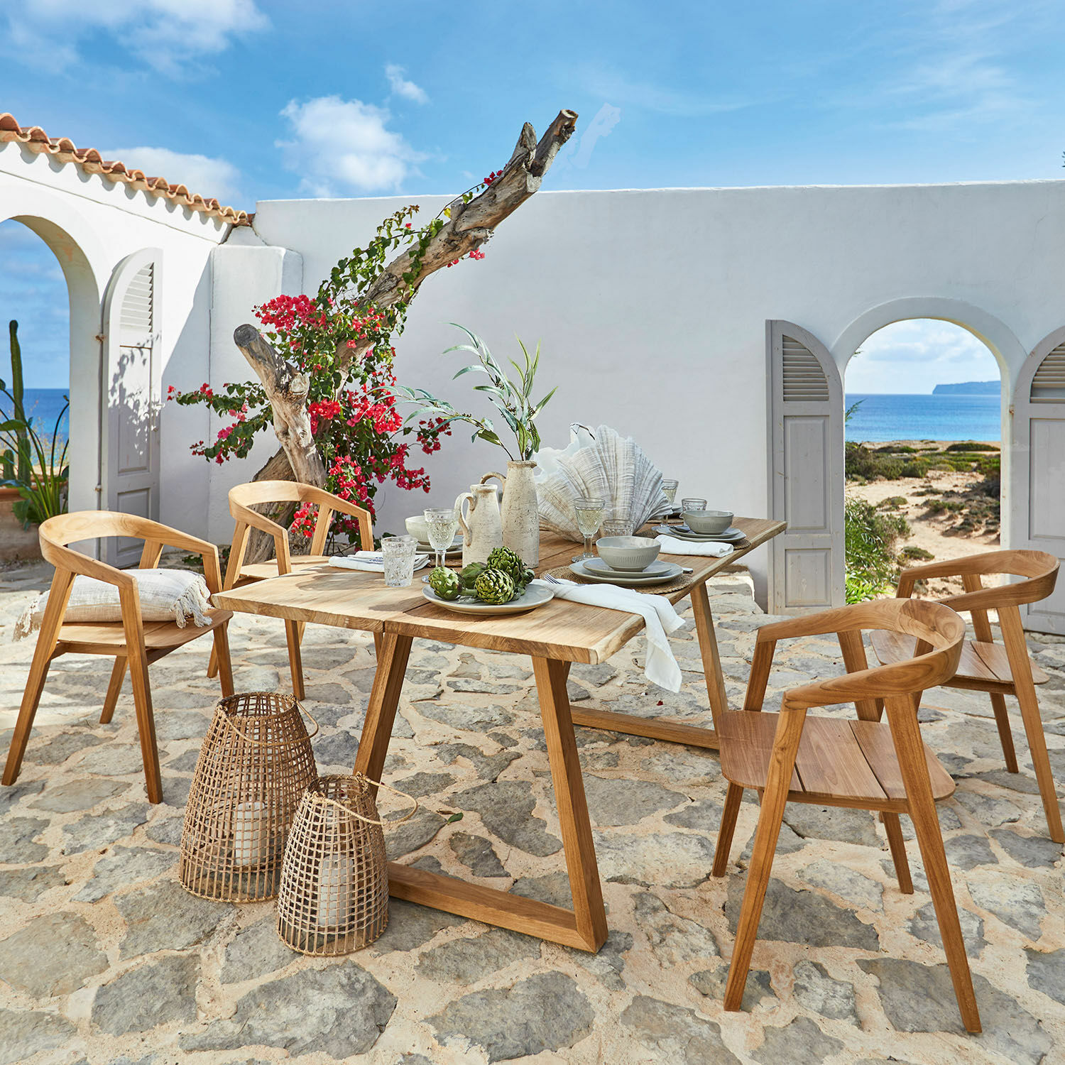Ensemble de mobilier de jardin en teck avec chaises et table sur patio en pierre face à la mer