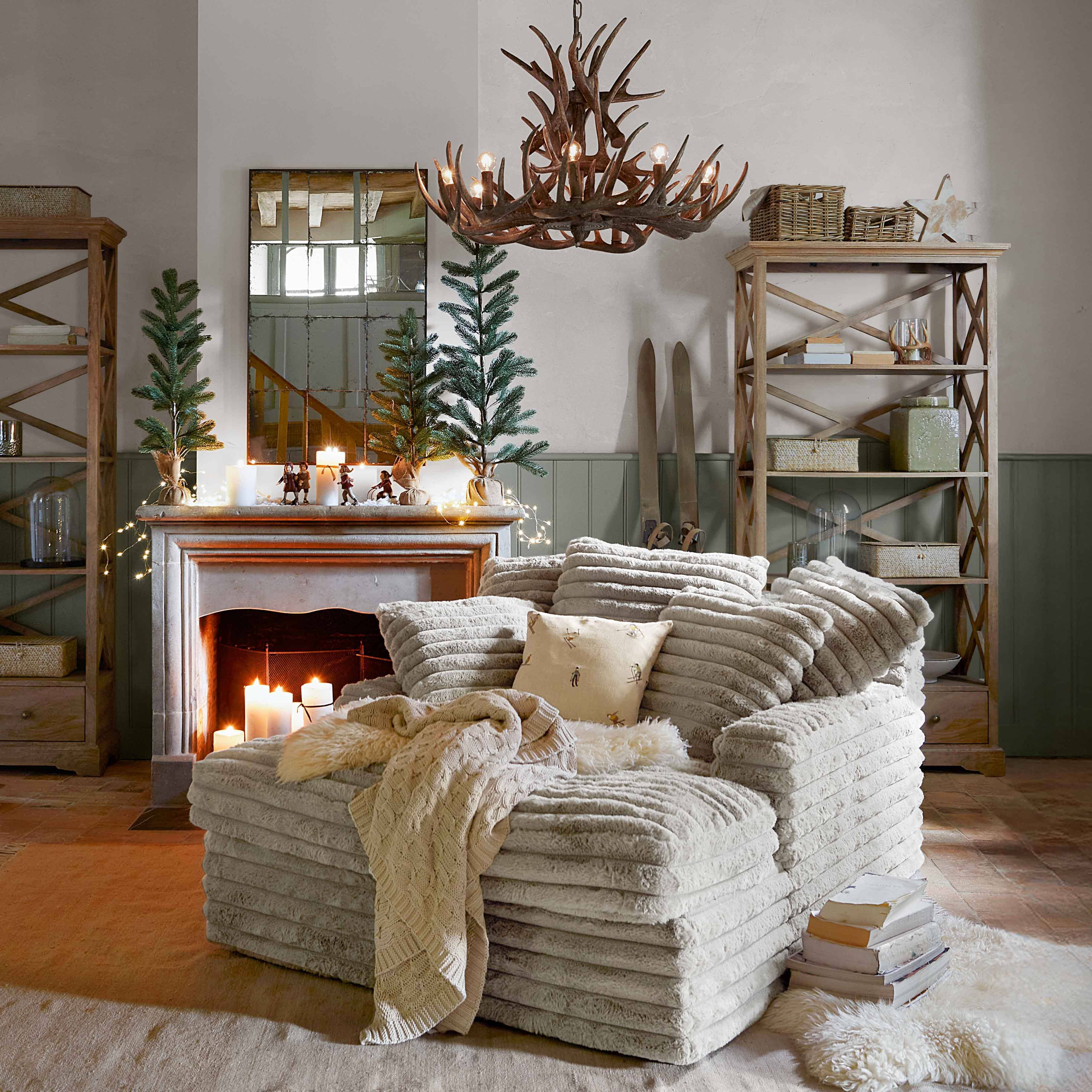 Fauteuil beige en tissu doux avec plaid et coussin dans un salon rustique avec cheminée et décorations festives