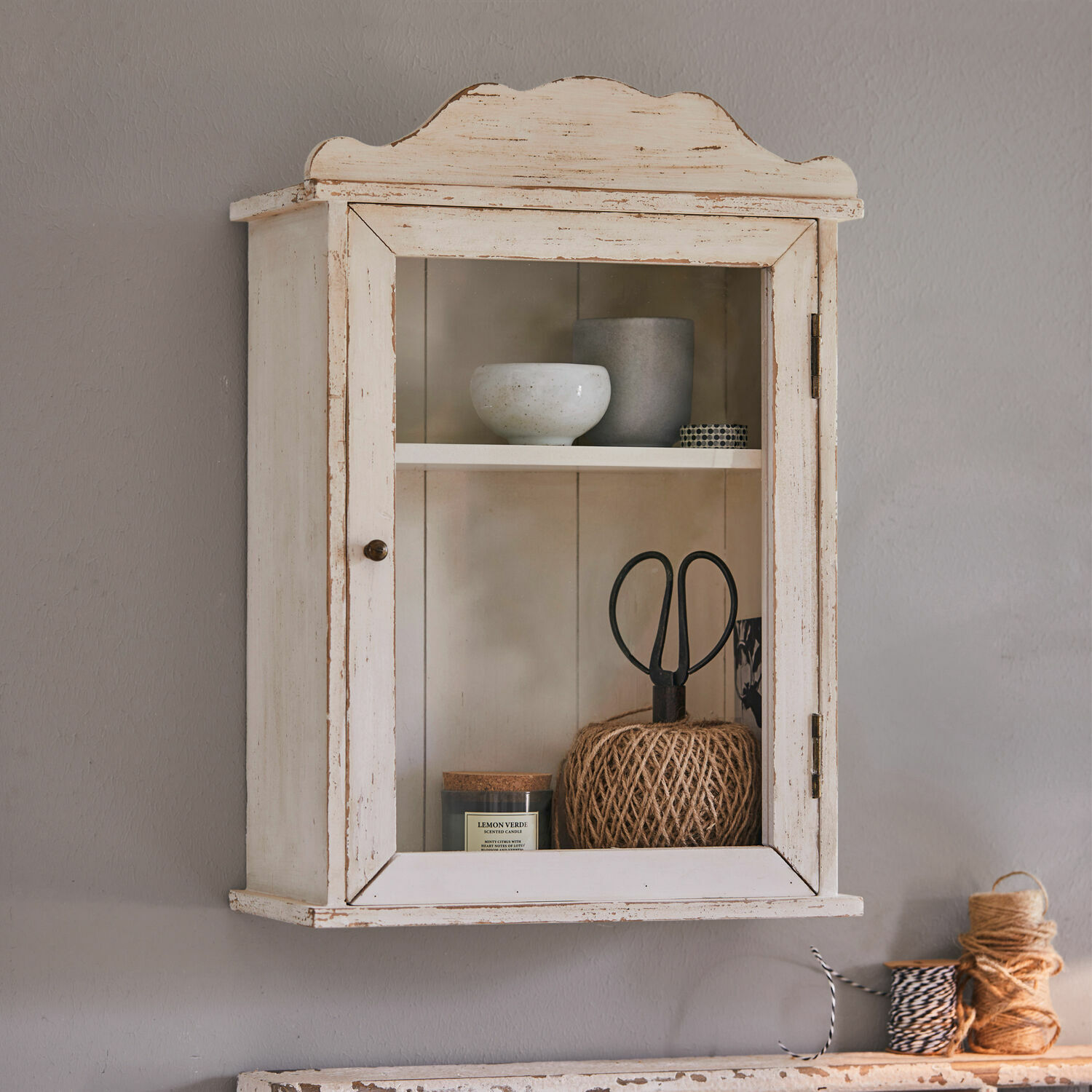 Meuble de rangement mural Sandrine Armoire murale en bois blanc vieilli avec porte vitrée et objets décoratifs à l'intérieur