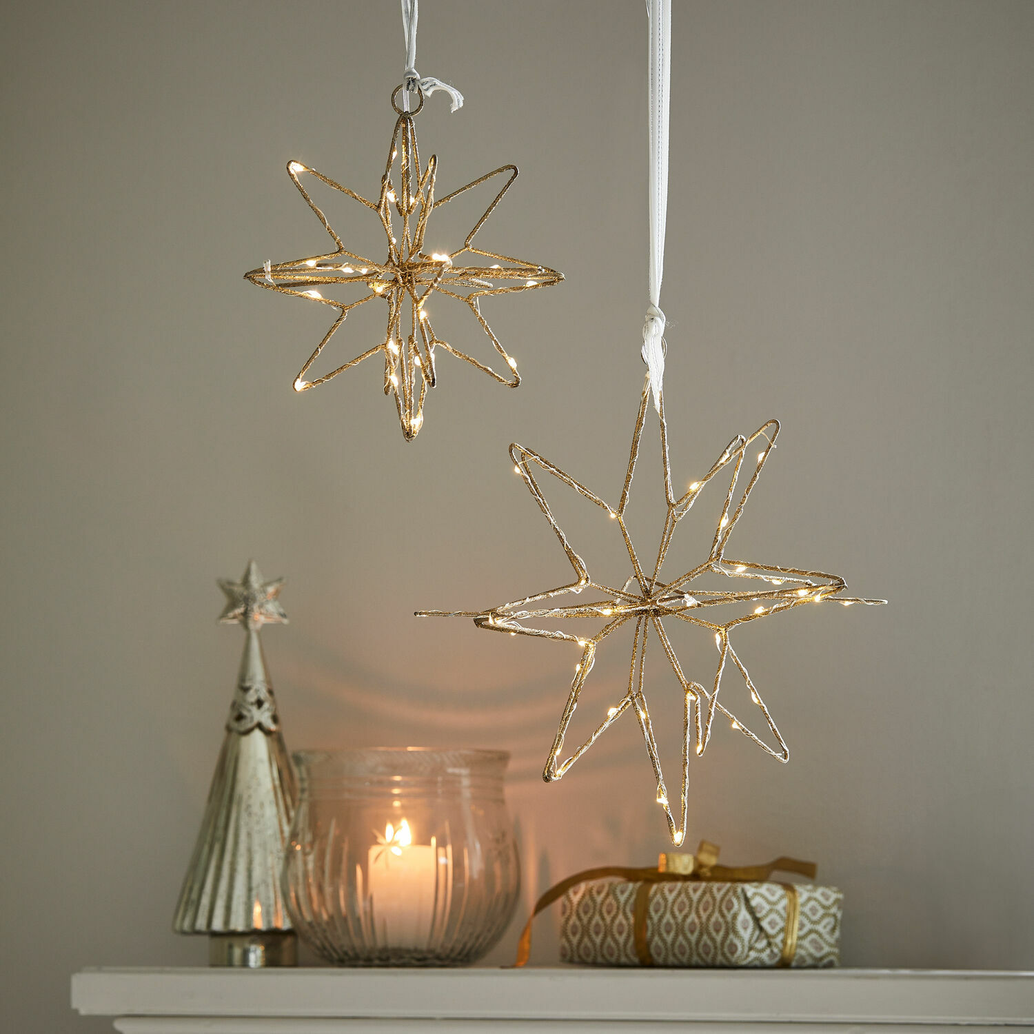 Lot de 2 étoiles LED Pérole Décorations étoiles dorées lumineuses suspendues au-dessus d'une bougie et d'un cadeau sur une étagère blanche