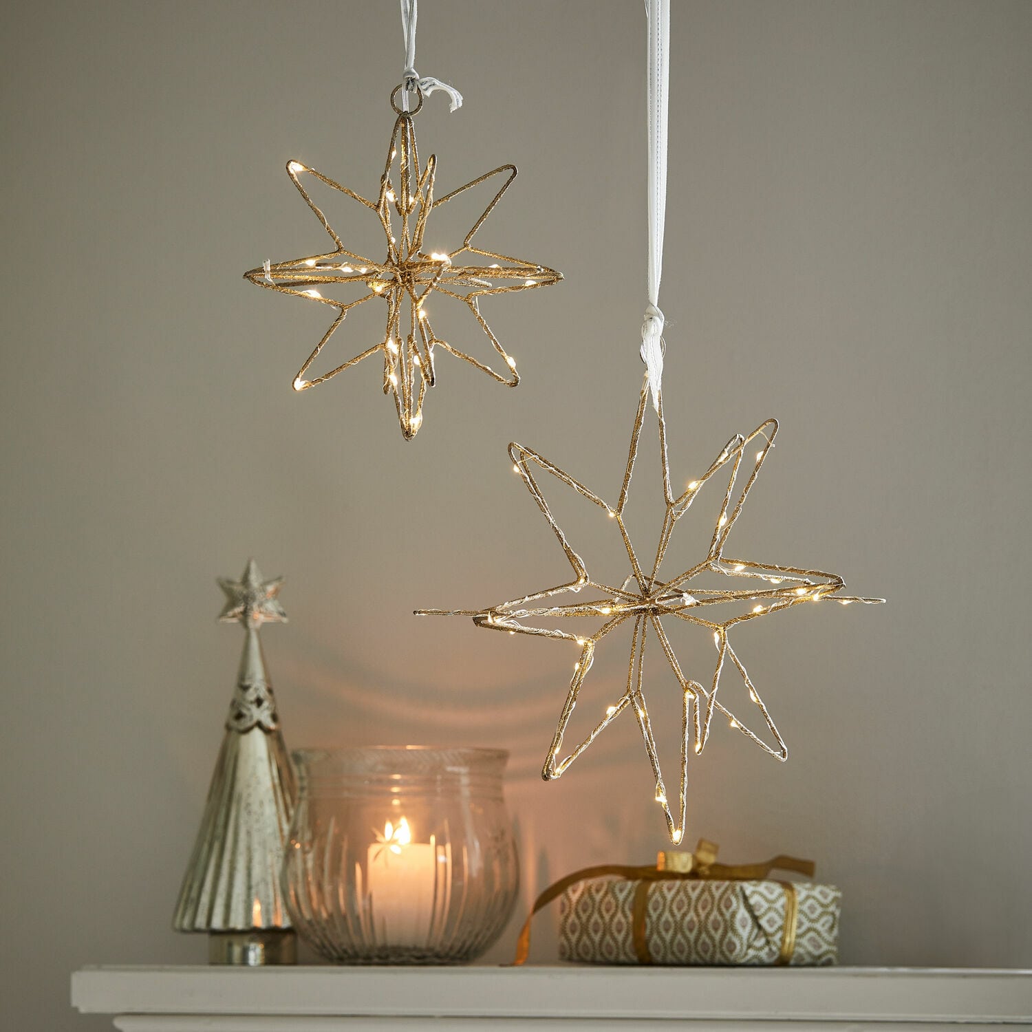 Lot de 2 étoiles LED Pérole Décorations étoiles dorées lumineuses suspendues au-dessus d'une bougie et d'un cadeau sur une étagère blanche