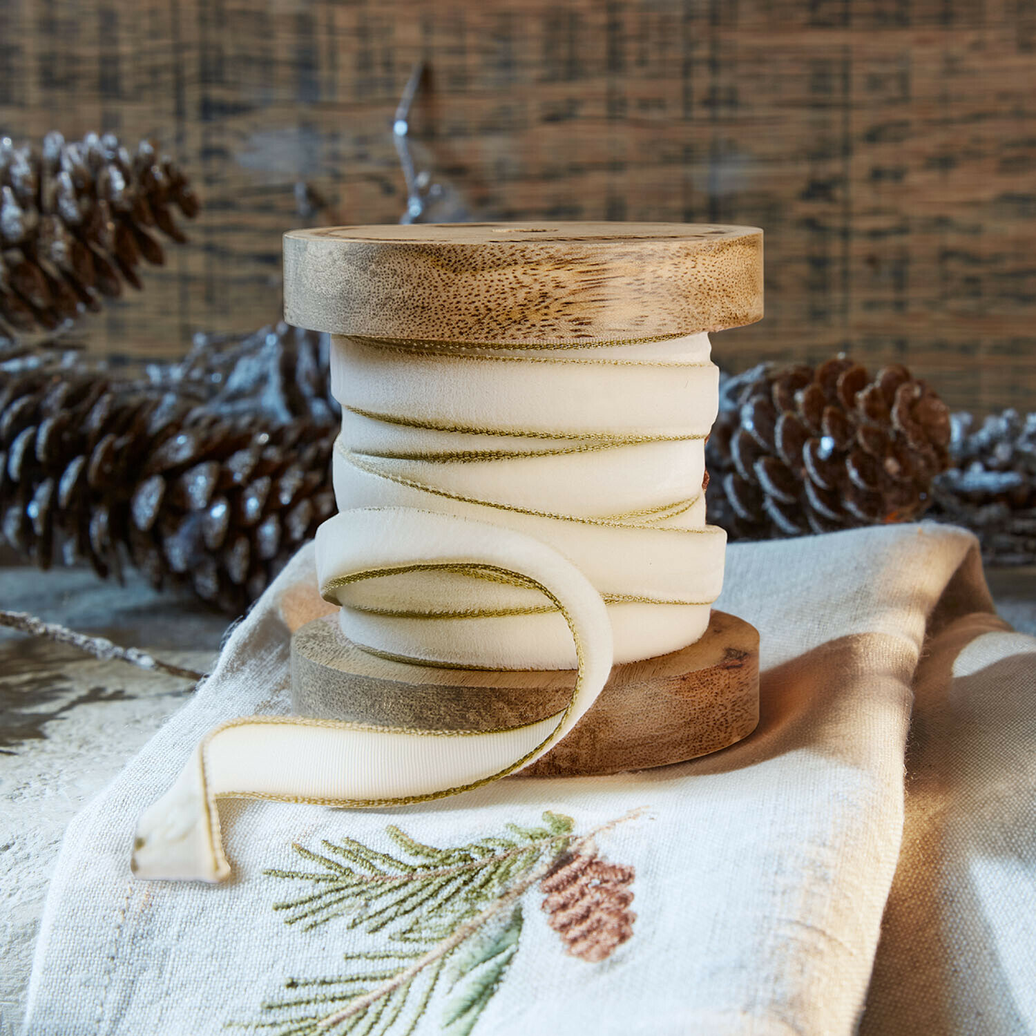 Ruban de velours Sorima Bobine en bois naturel avec ruban crème bordé de vert sur tissu en lin brodé d’un motif de pomme de pin