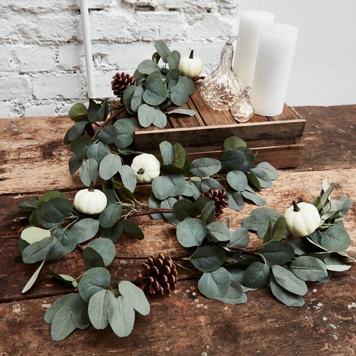 Guirlande décorative en feuilles d'eucalyptus vertes, petites citrouilles blanches et pommes de pin sur table en bois
