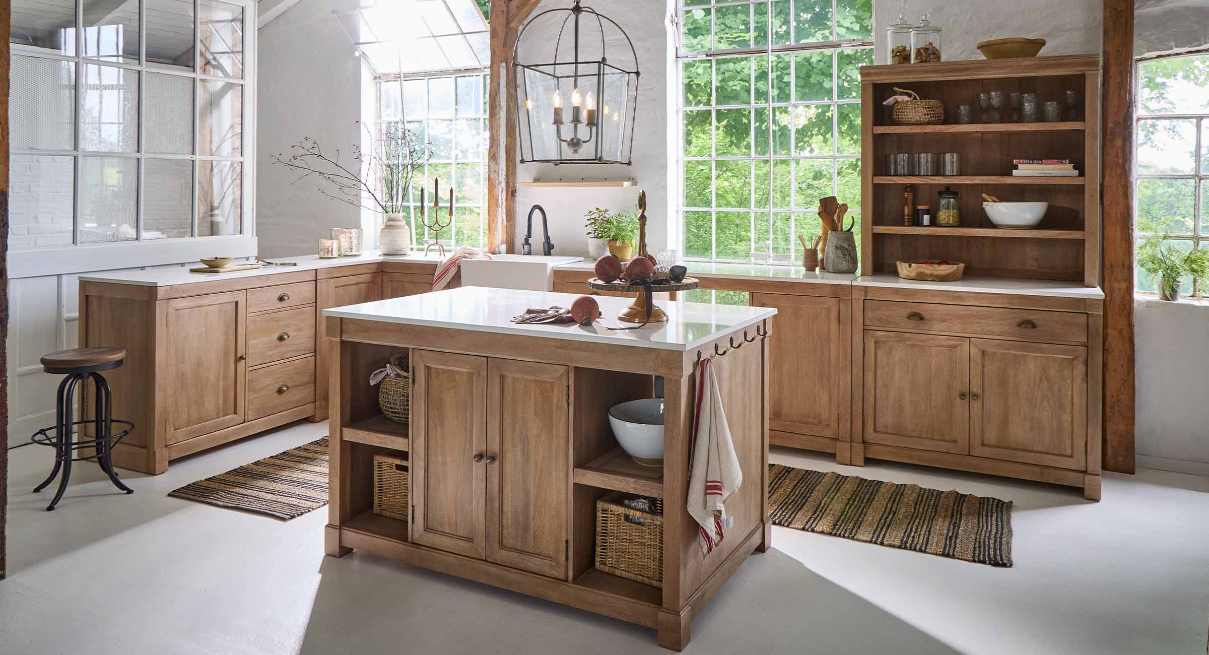 Cuisine avec îlot et meubles en chêne naturel, plans de travail blancs et grandes fenêtres lumineuses