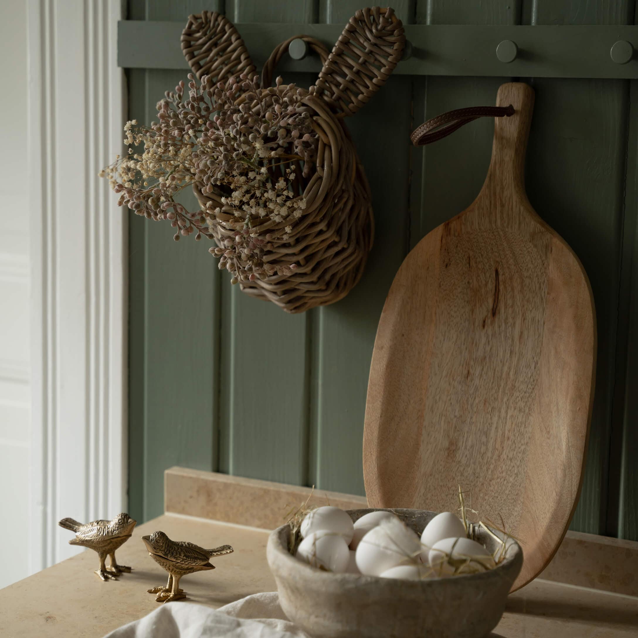 Panier en osier en forme de lapin avec fleurs séchées et planche à découper en bois sur fond vert