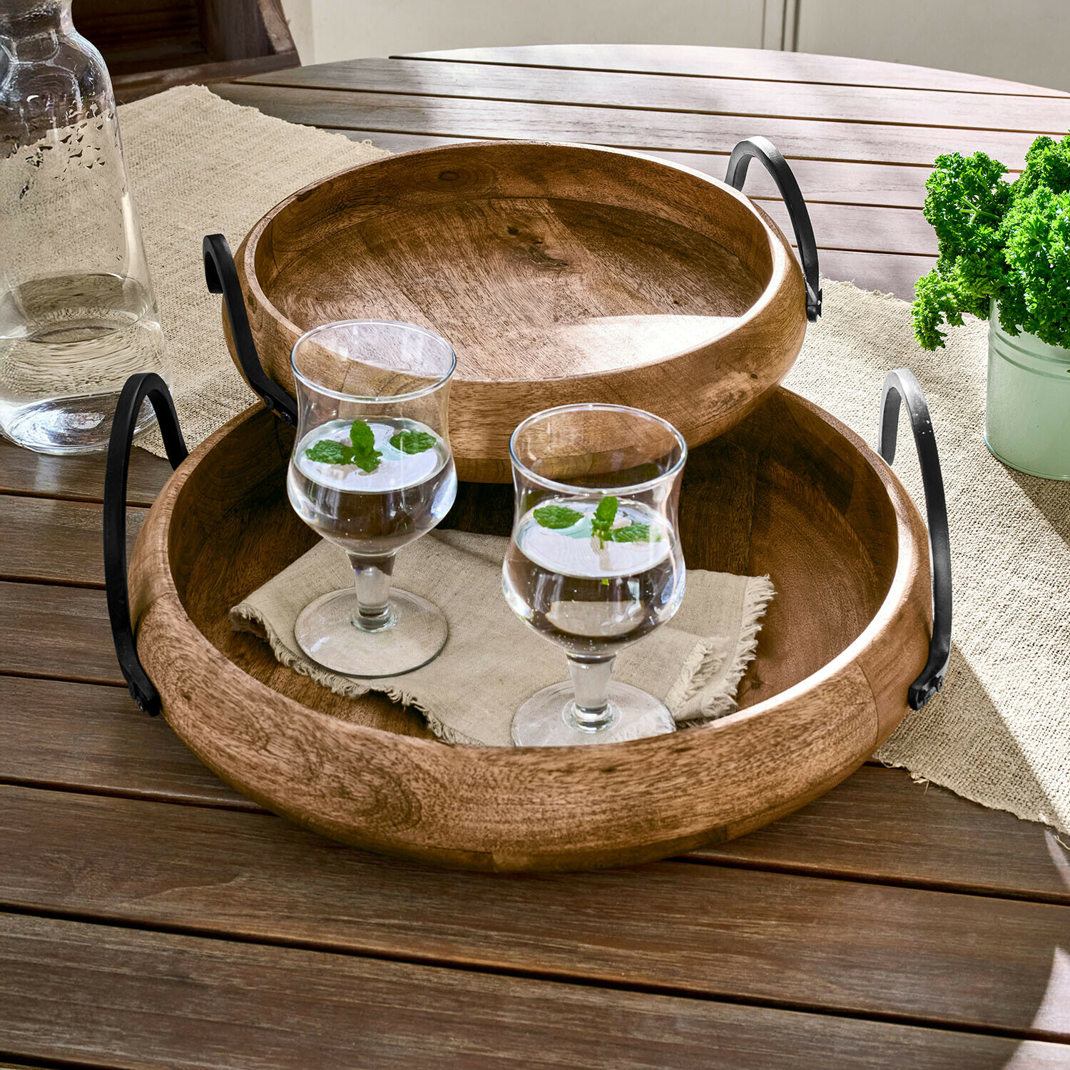 Lot de 2 plateaux Arémont Plateaux ronds en bois avec poignées en métal sur table en bois avec deux verres d'eau à la menthe