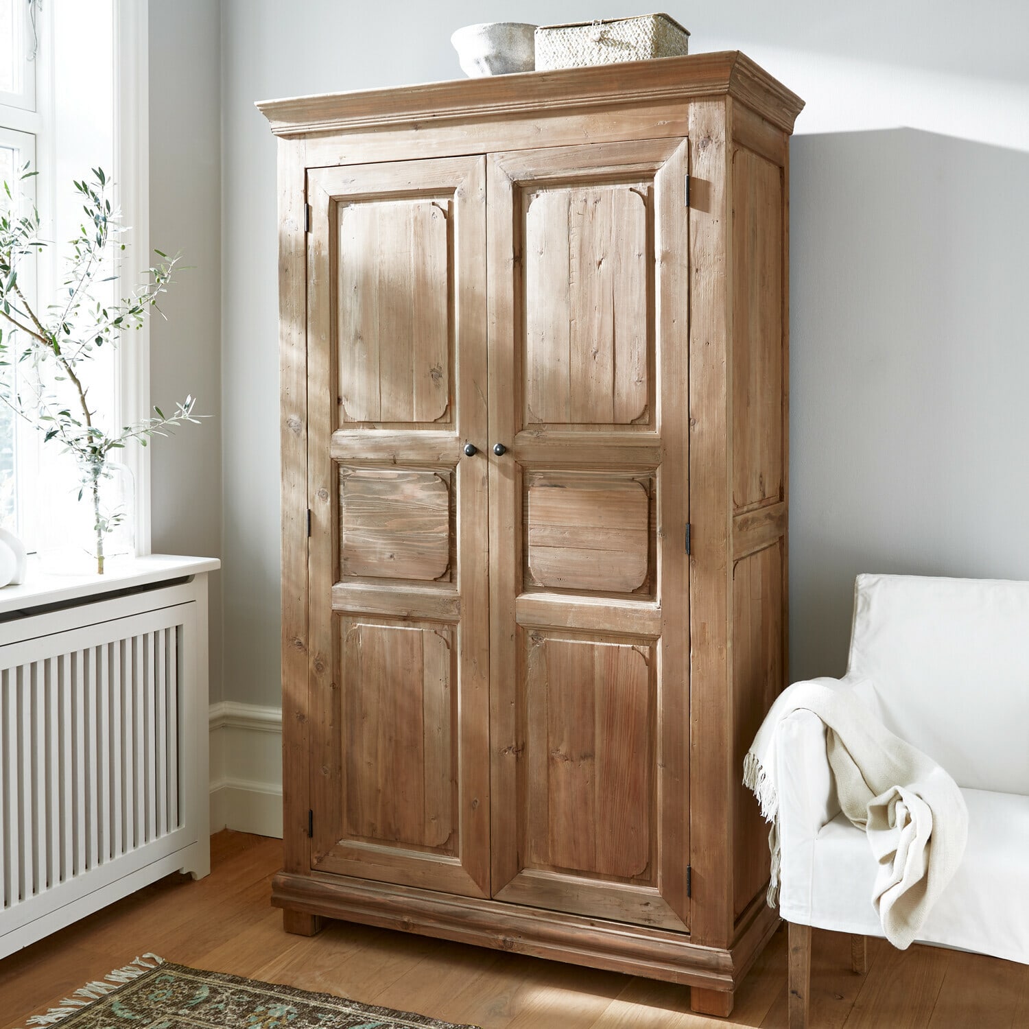 Armoire Gavrielle Armoire en bois naturel dans une pièce lumineuse avec fauteuil blanc et tapis décoratif
