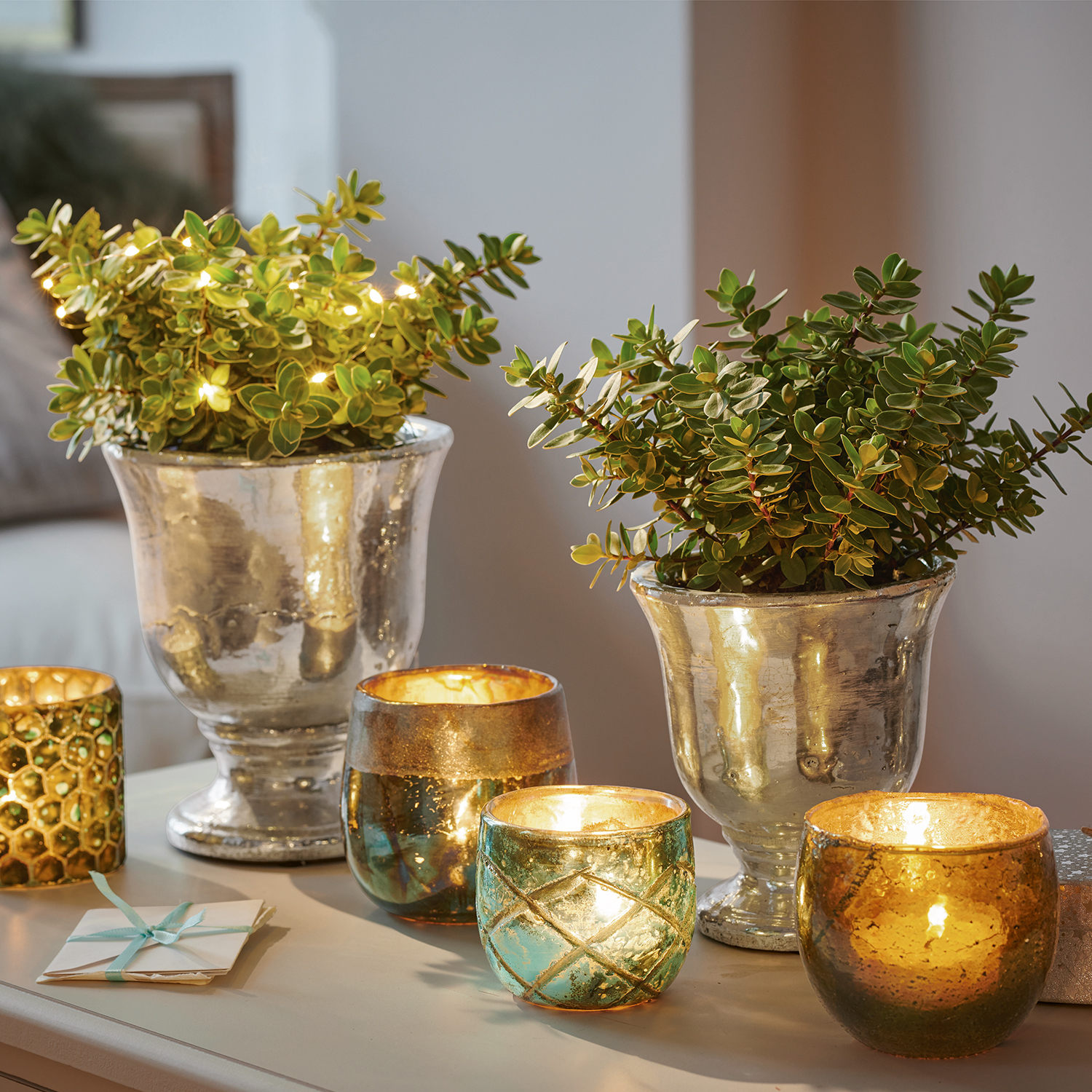 Pots argentés décoratifs avec plantes vertes et photophores en verre lumineux sur une table