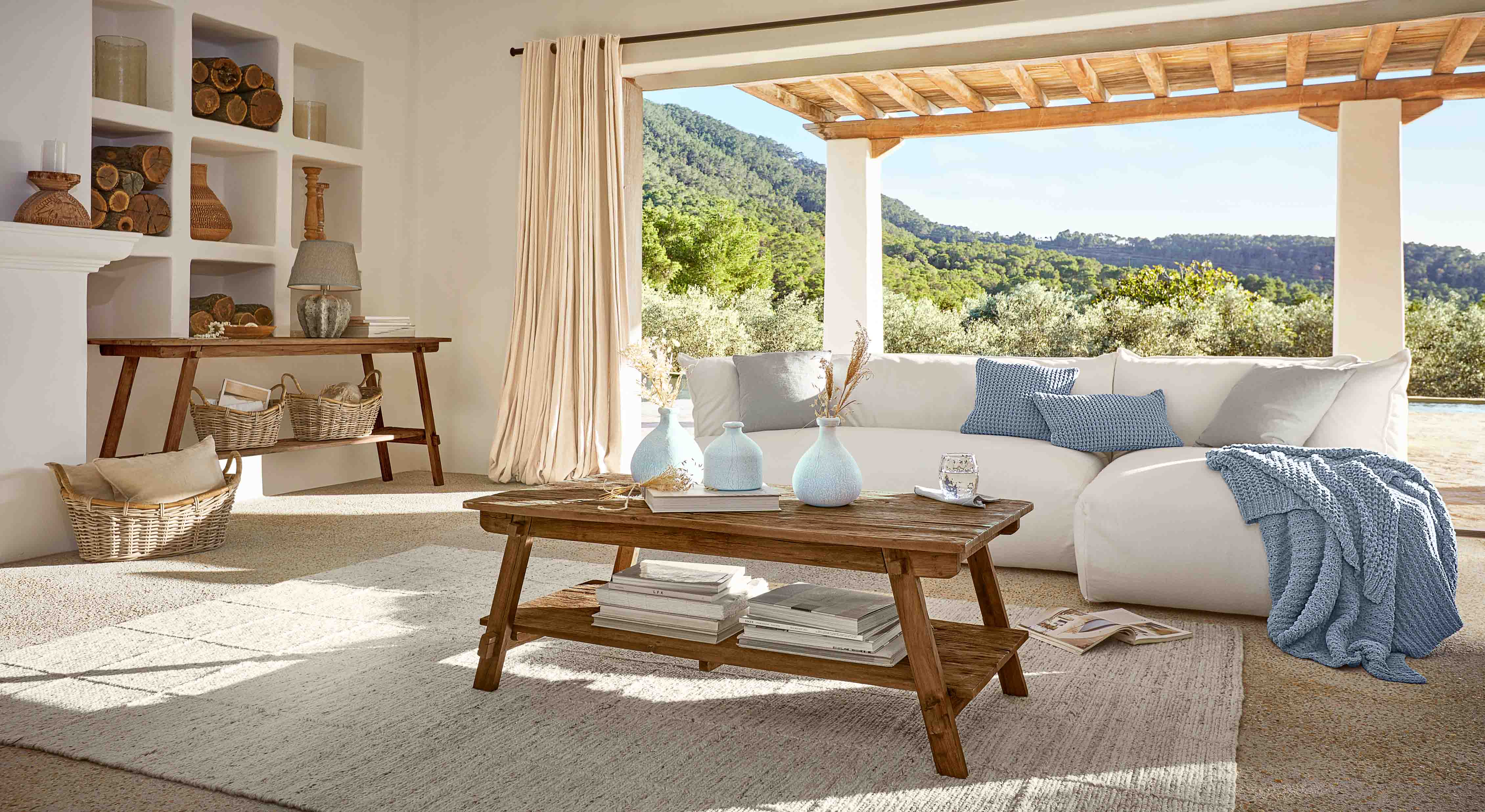 Salon lumineux avec table basse en bois, canapé blanc et plaid bleu, décor naturel et vue sur la nature