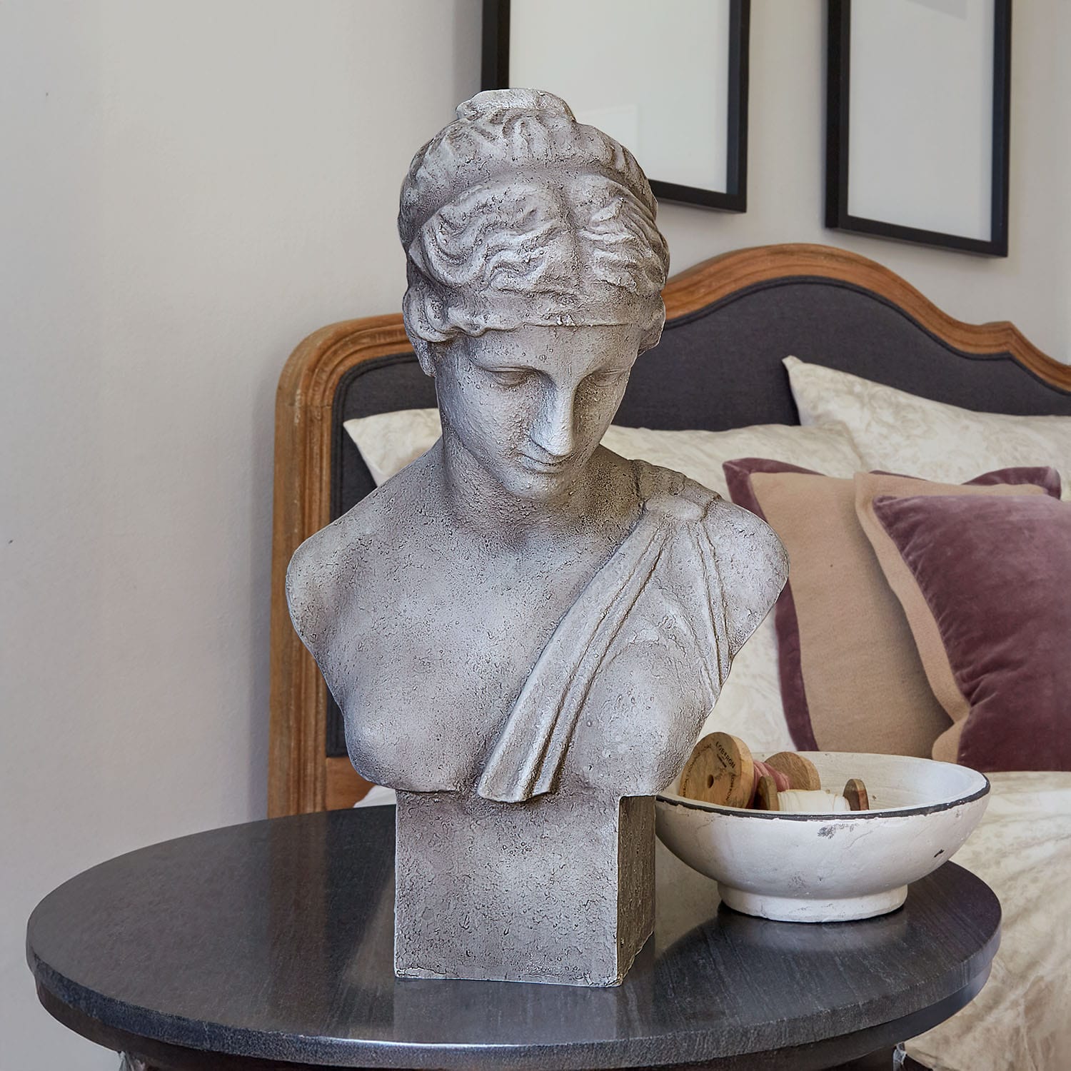 Buste en pierre grise sur une table noire dans une chambre élégante avec coussins décoratifs