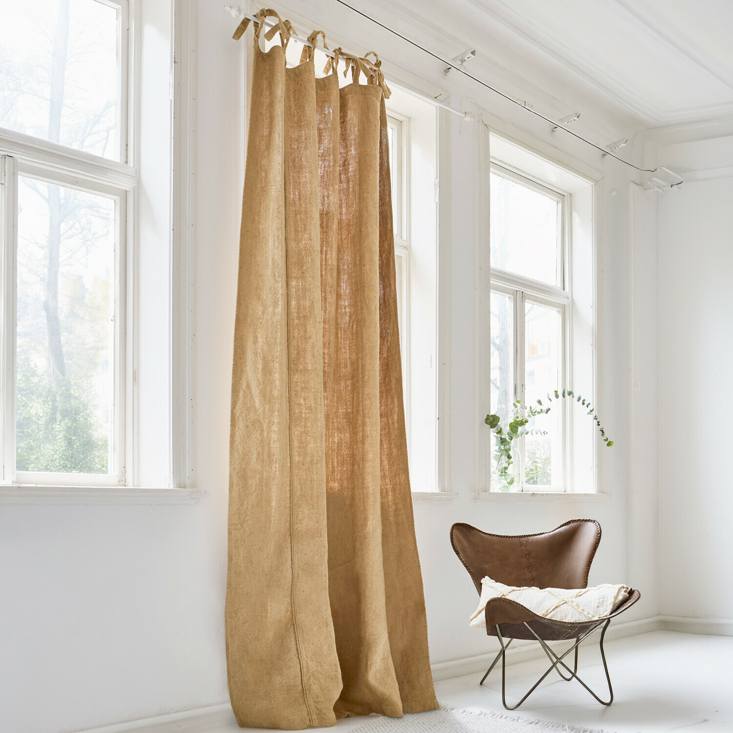 Rideau beige en lin naturel dans une pièce lumineuse avec une grande fenêtre et un fauteuil marron