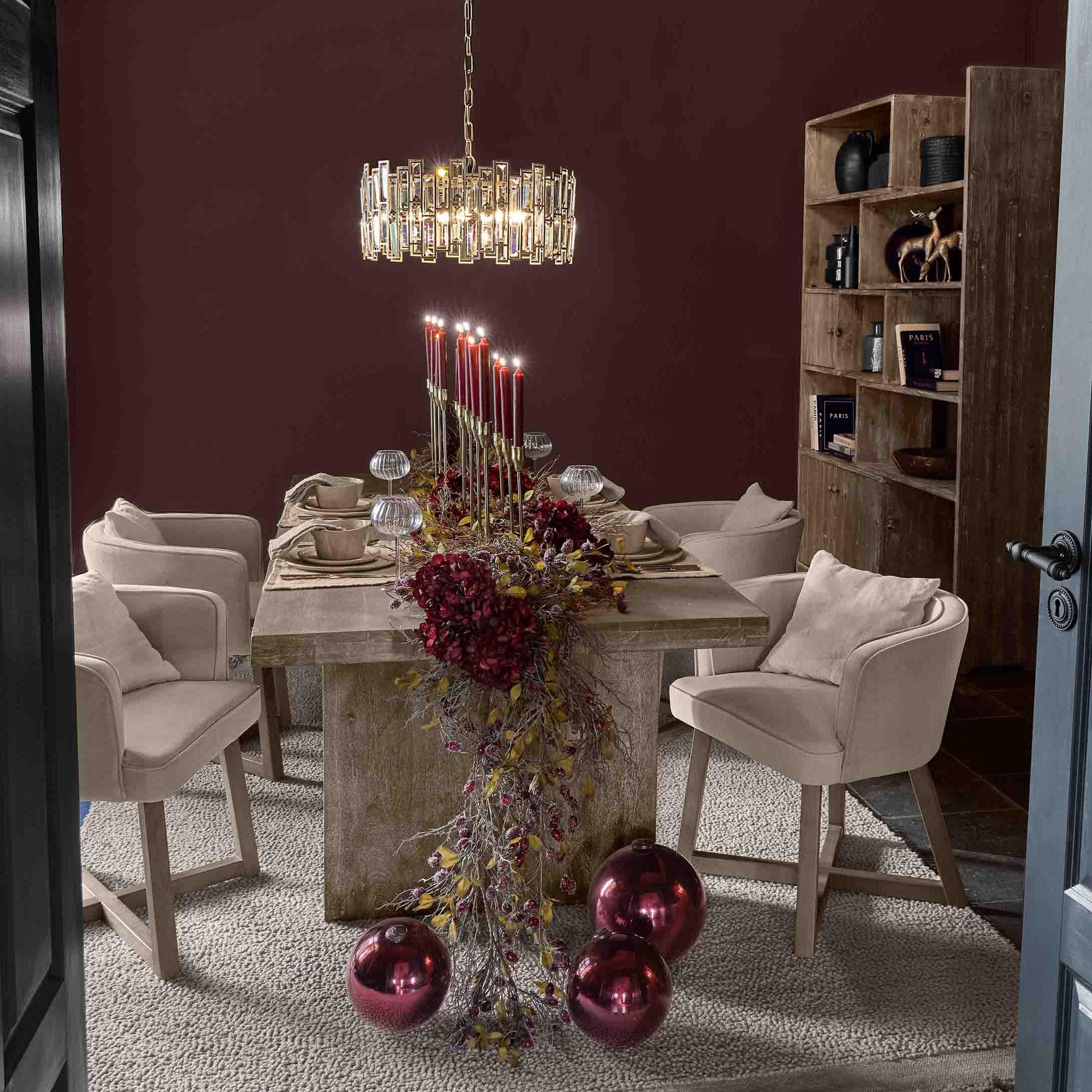 Salle à manger avec table en bois, chaises beige et décoration de bougies rouges et boules de Noël brillantes