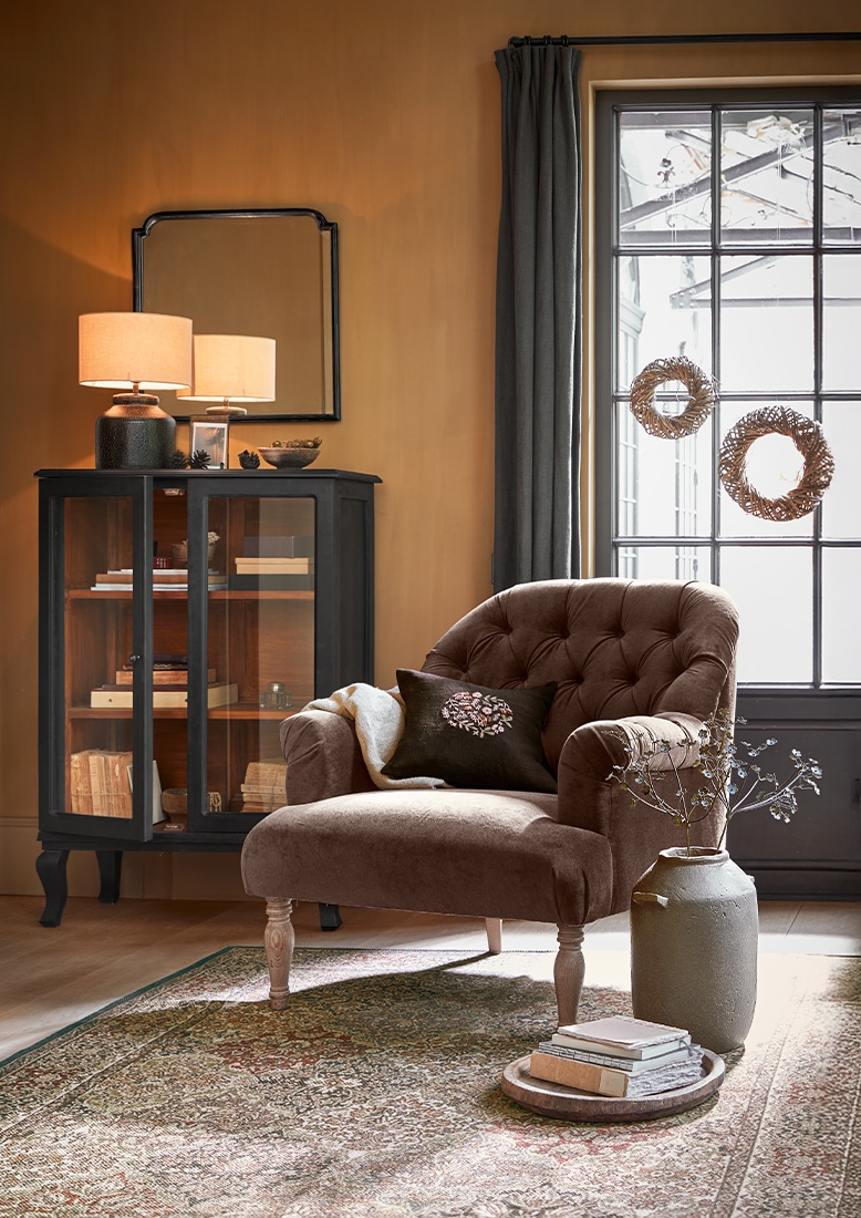 Fauteuil rembourré marron avec coussin et meuble gris avec lampe dans un salon chaleureux avec tapis