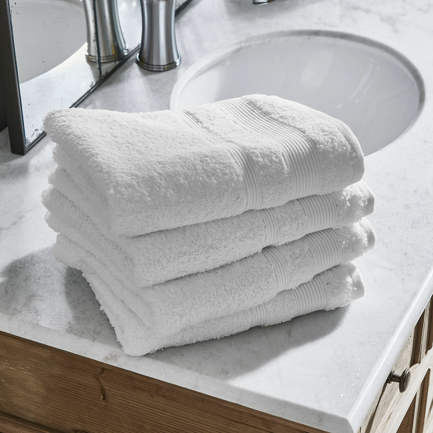 Lot de 4 serviettes Bourogne Serviettes blanches en coton empilées sur un comptoir en marbre dans une salle de bain moderne