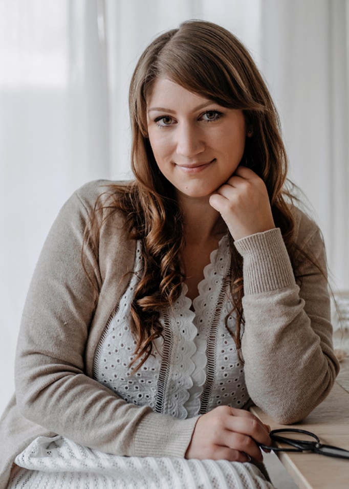 Femme en cardigan beige et blouse blanche en dentelle assise à une table avec des ciseaux pour emballage cadeau